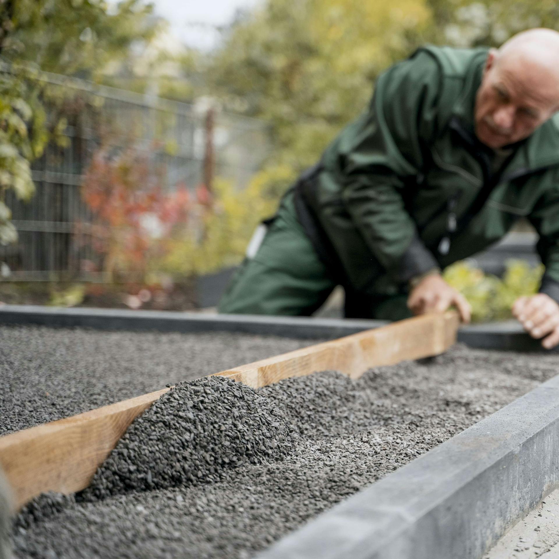 Gärtner verteilt Edelsplit mithilfe eines Brettes gleichmäßig über der Tragschicht.