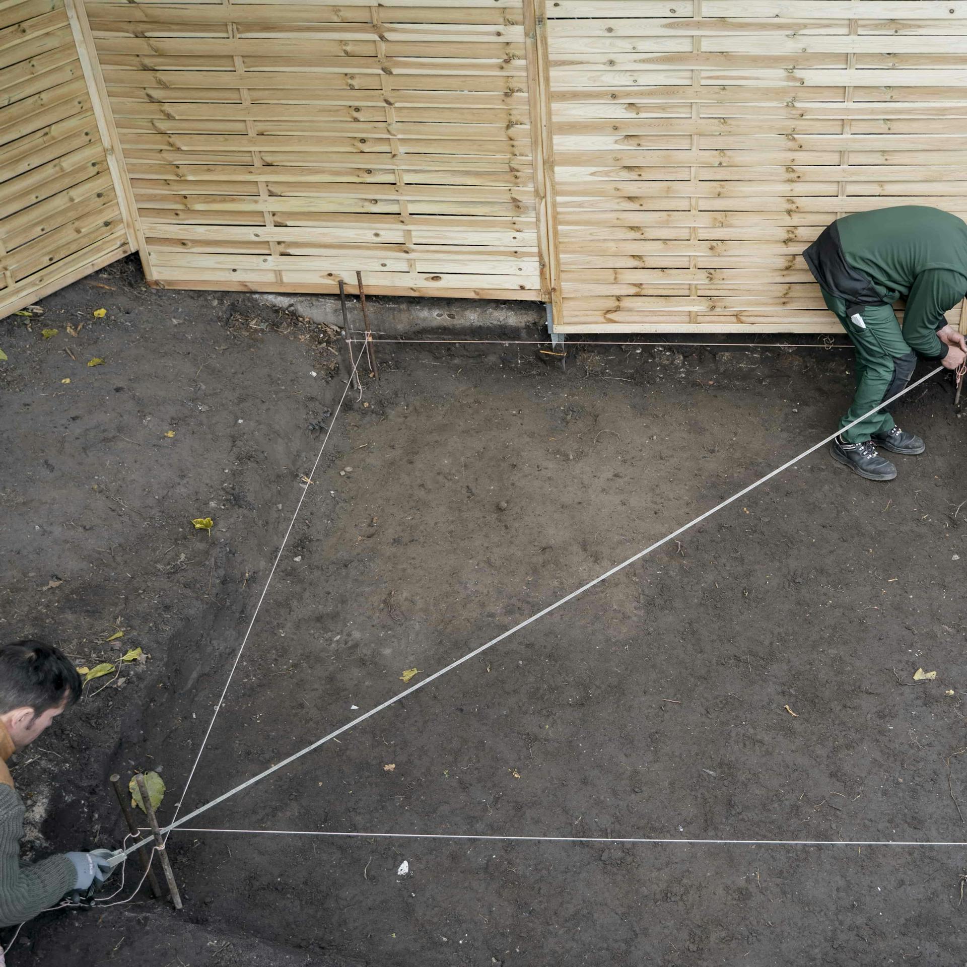 Zwei Handwerker spannen Maurerschnur für ein Plattenfundament.