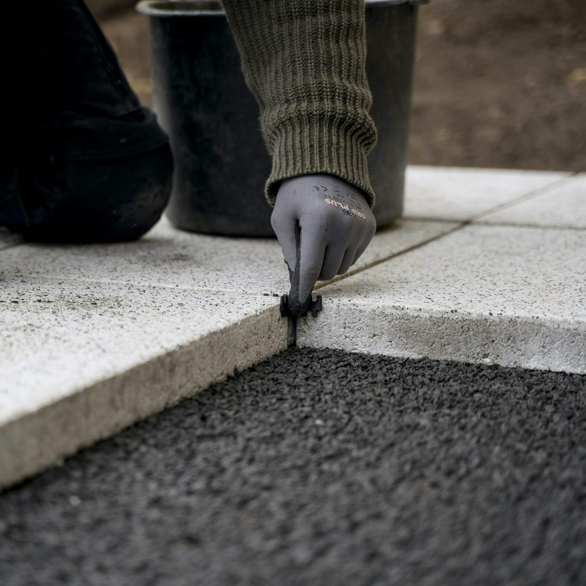 Handwerker mit Handschuhen verlegt Gehwegplatten für das Plattenfundament.