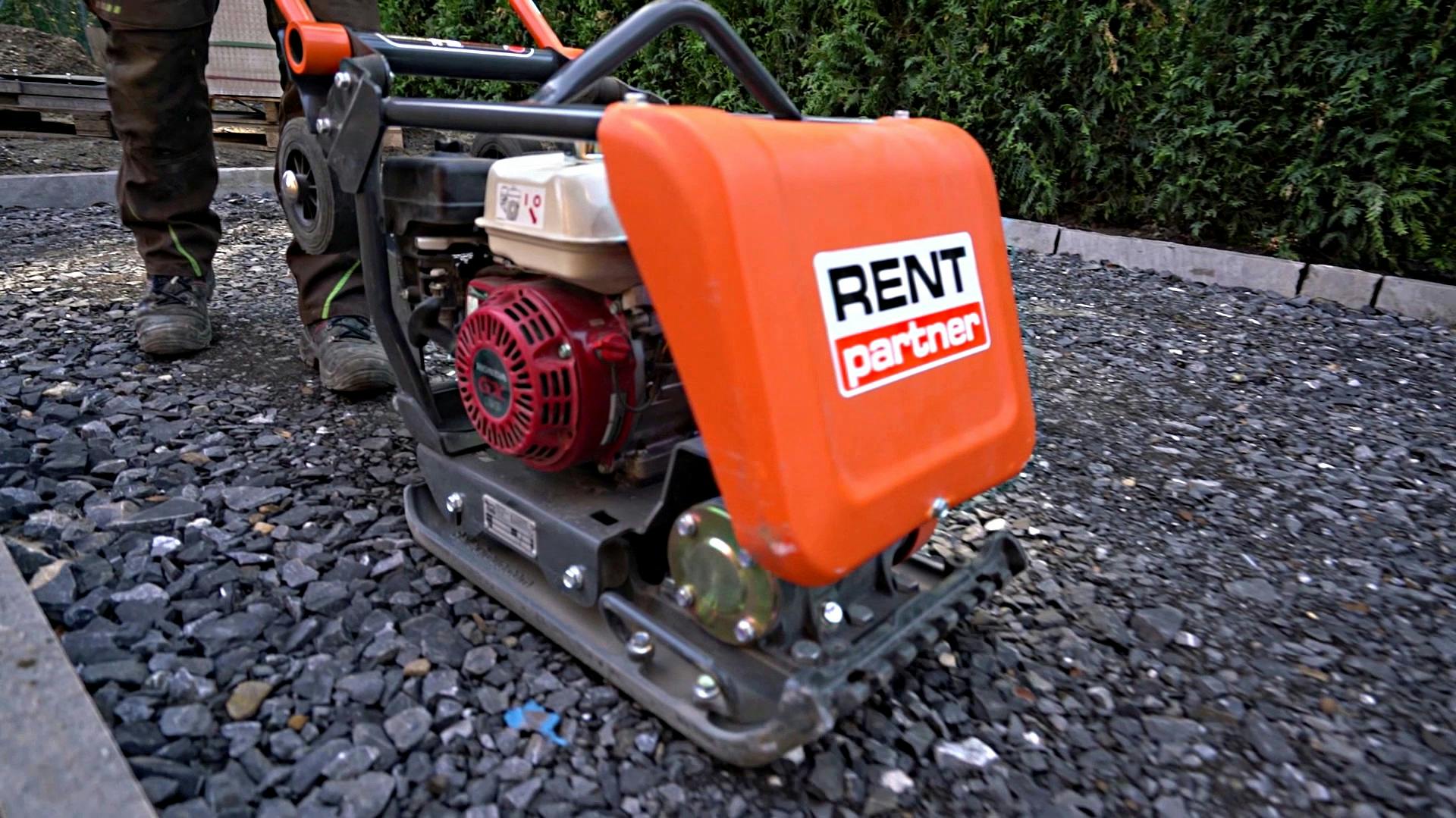 Foto einer Rüttelplatte, die von einem Handwerker auf Schotter angewendet wird