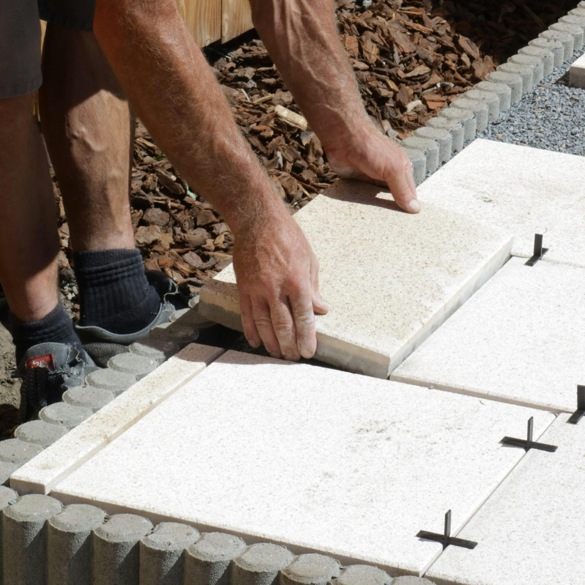 Pracovník ukladá obdĺžnikové dosky z prírodného kameňa do štrkového lôžka na chodník v záhrade.