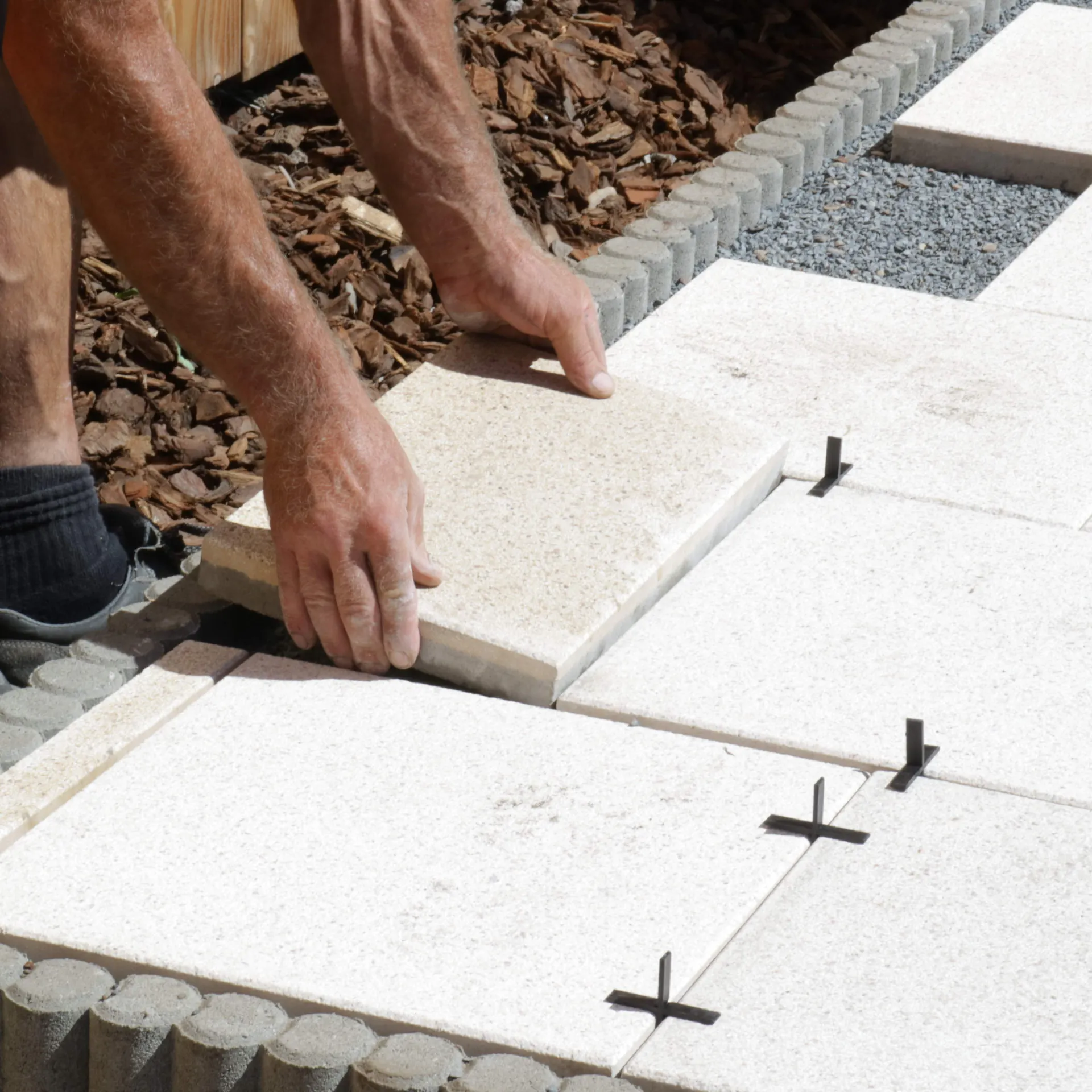 Jemand verlegt Terrassenplatten auf einem Splittbett.