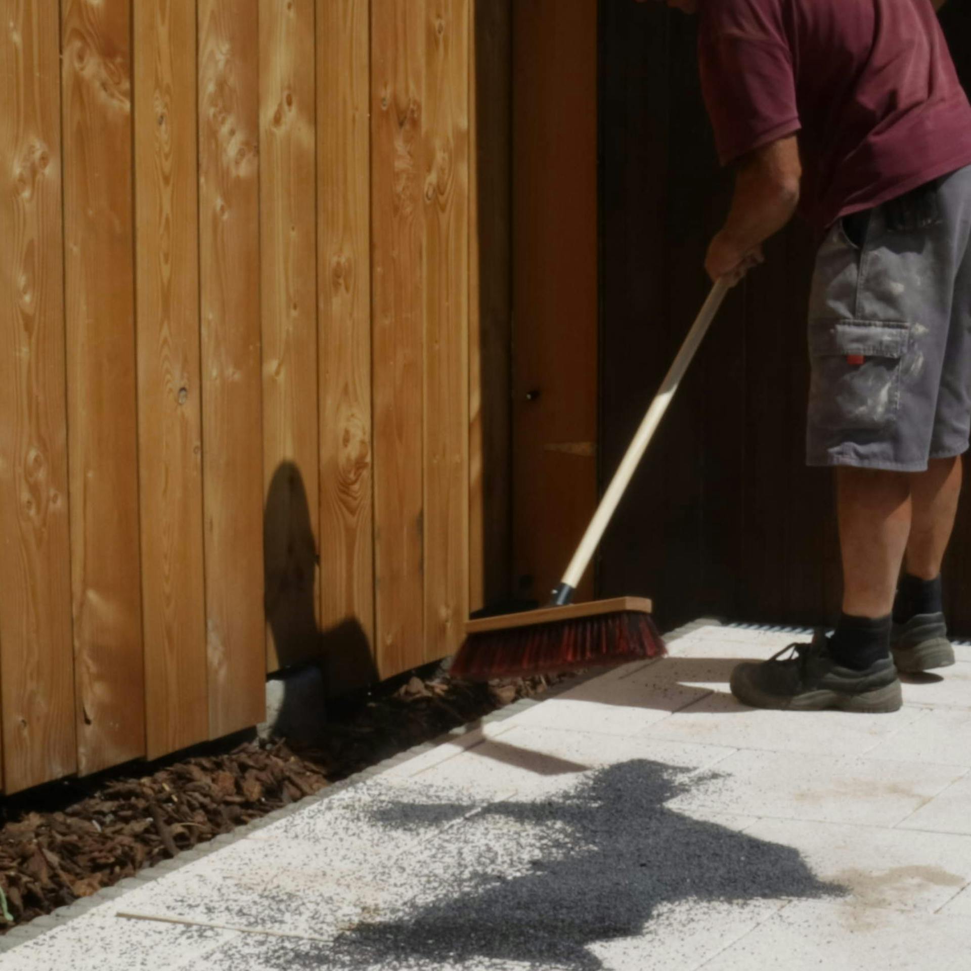 Osoba metlou rozdeľuje škárovací piesok medzi terasové dosky z kameňa.