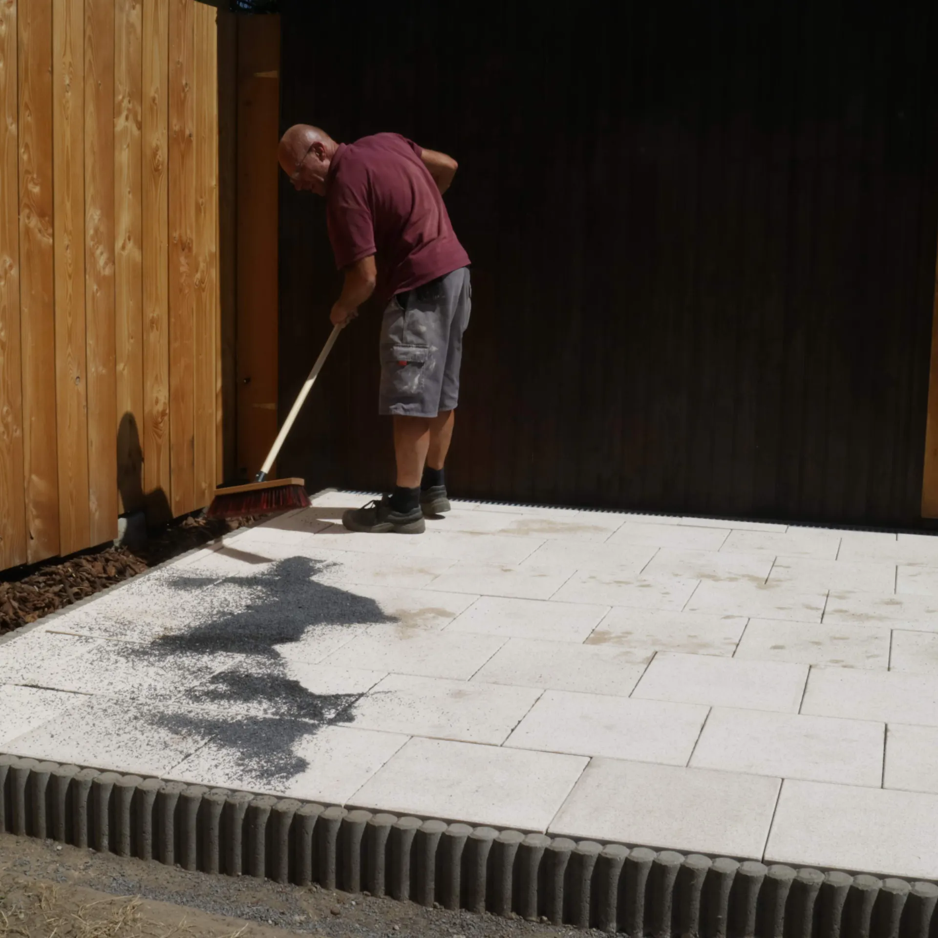 Heimwerker bringt Fugenmaterial mit dem Besen in die Terrassenfugen ein.