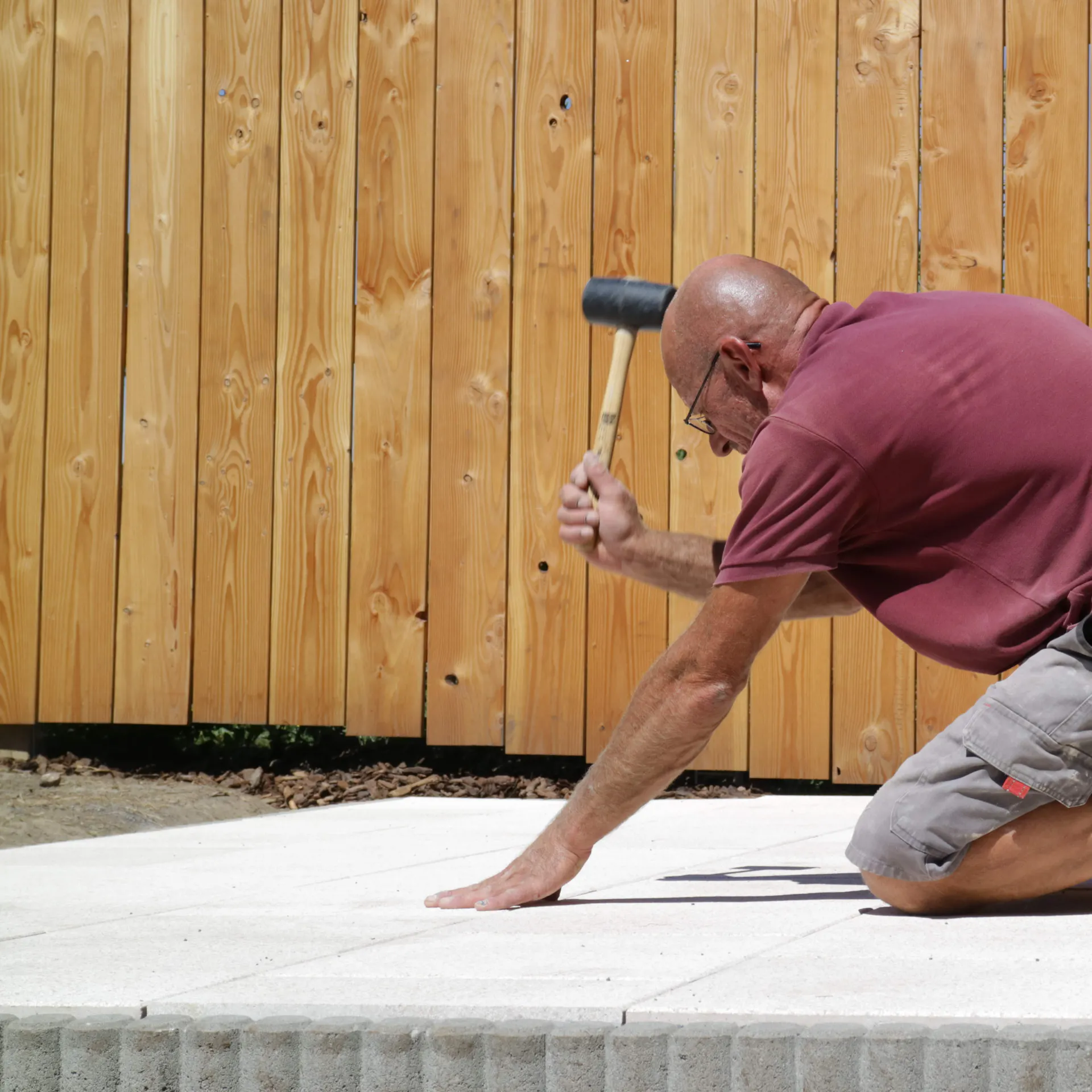 Heimwerker schlägt Terrassenplatte mit Gummihammer an.