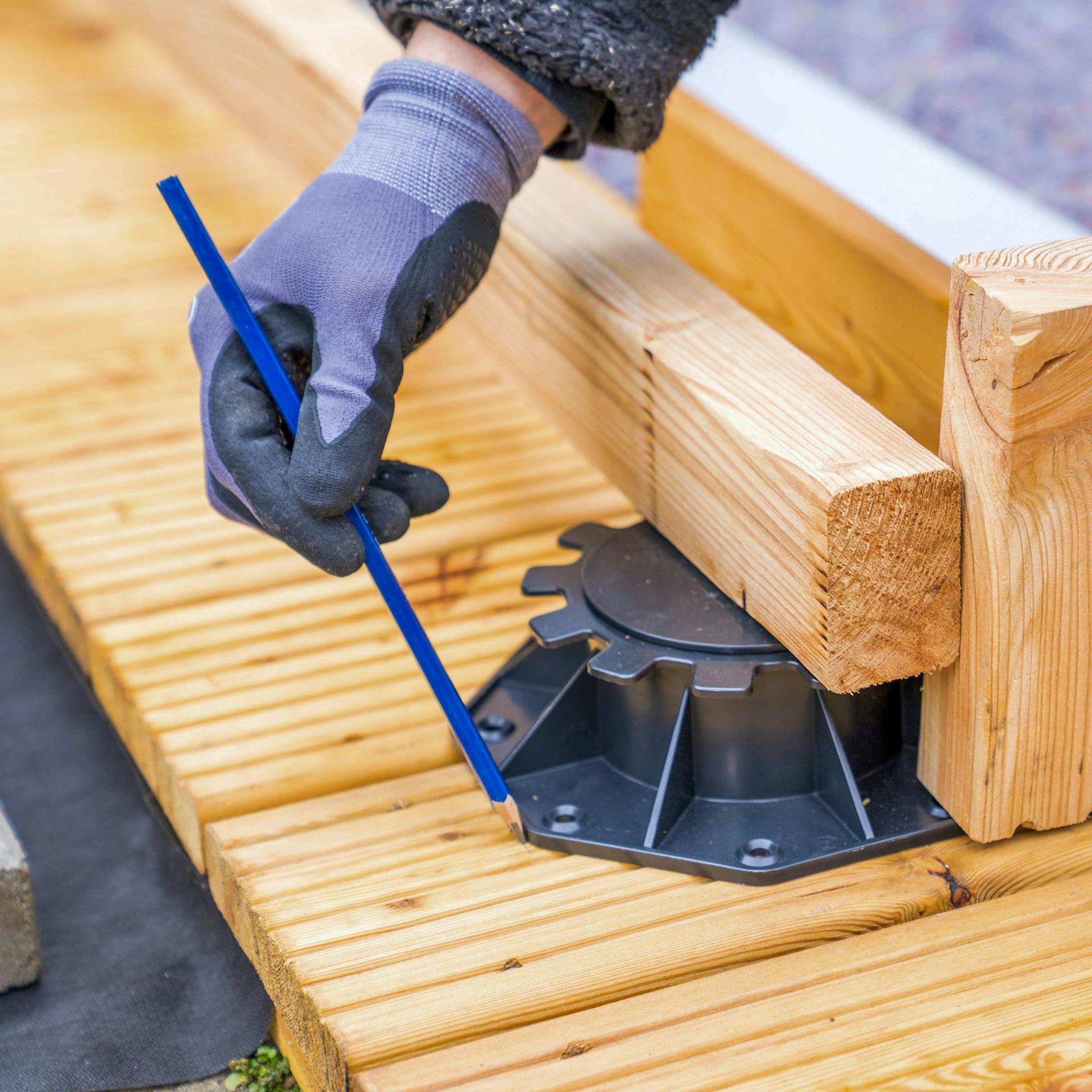 Eine Hand zeichnet die Position eines Stellfußes auf einer Terrasse ein.