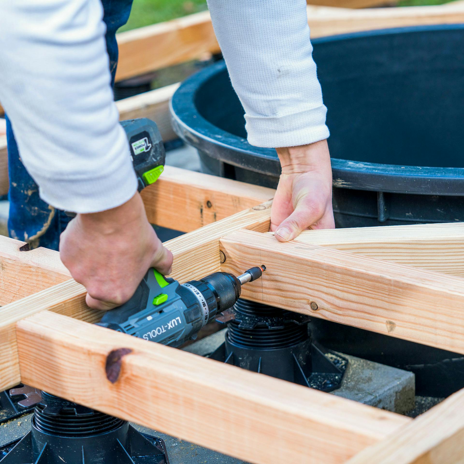 Zwei Hände schrauben eine Querstrebe neben einem Teichbecken fest.