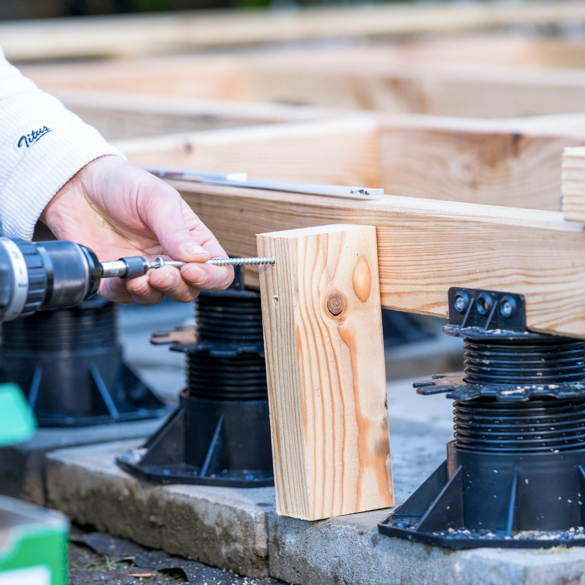 Hände schrauben einen Holzpfosten an einem Holzbalken fest