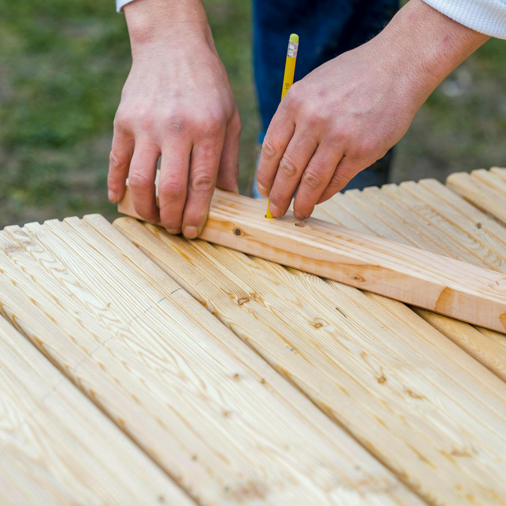 Hände zeichnen mithilfe eines Zirkels auf Terrassendielen.