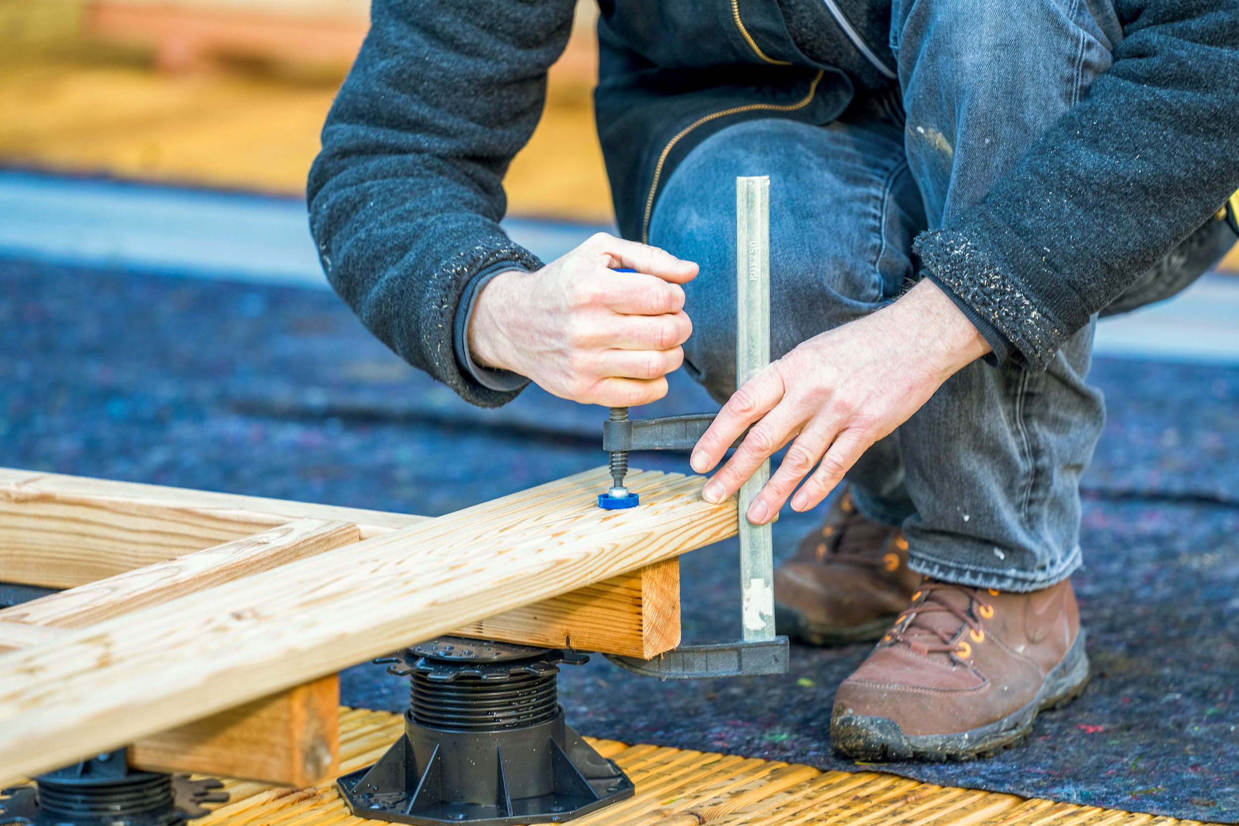 Mani fissano un’asse per terrazza a una trave di legno con un morsetto a vite.