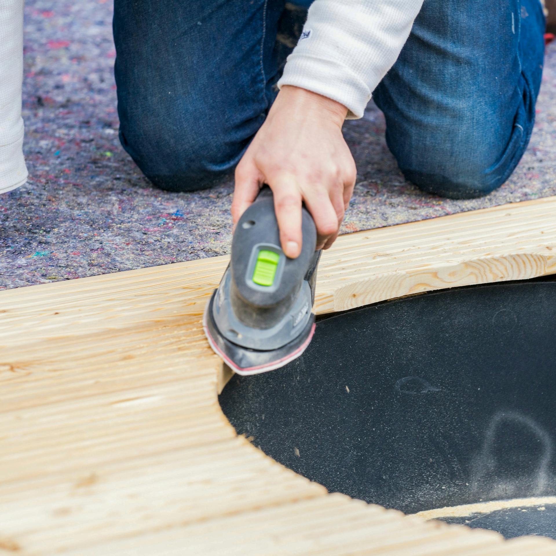 Eine Hand schleift die Kanten an Terrassendielen ab.