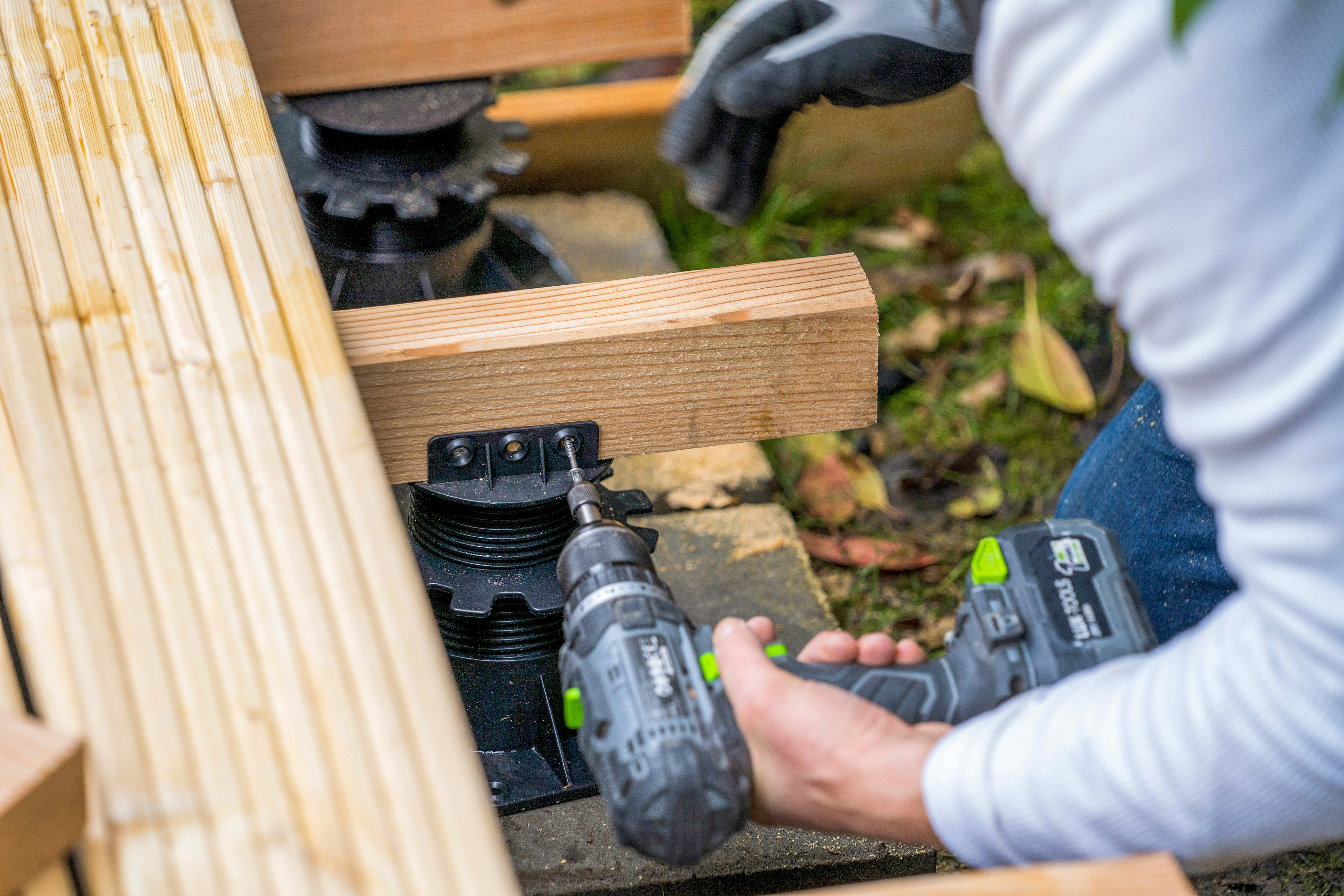 Una mano avvita un piede di appoggio a una trave di legno.