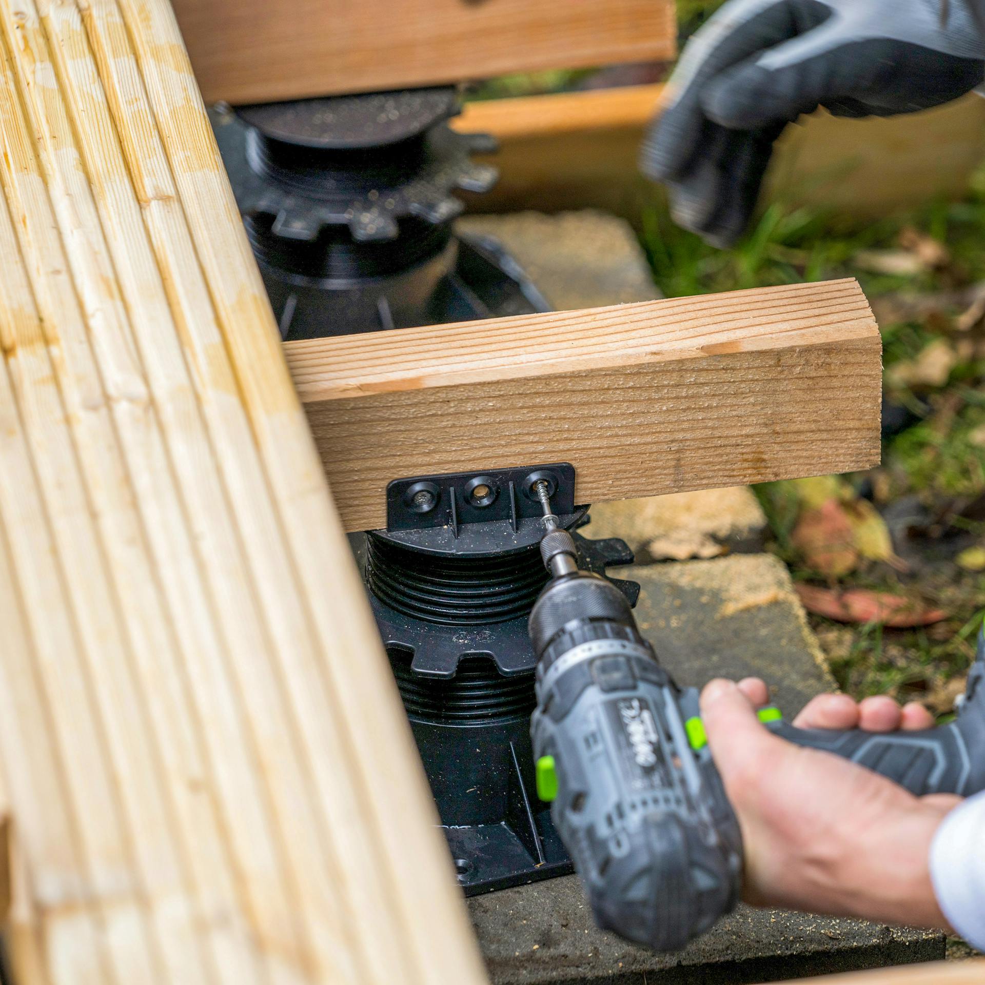 Eine Hand schraubt einen Stellfuß an einen Holzbalken.
