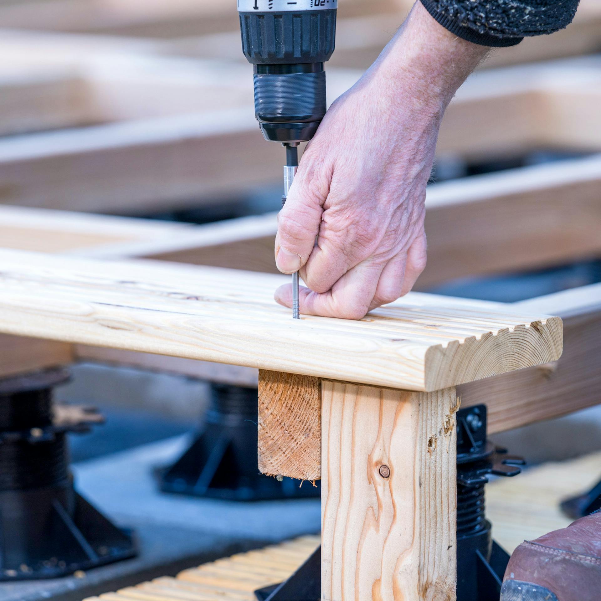 Eine Hand schraubt eine Terrassendiele auf eine Unterkonstruktion