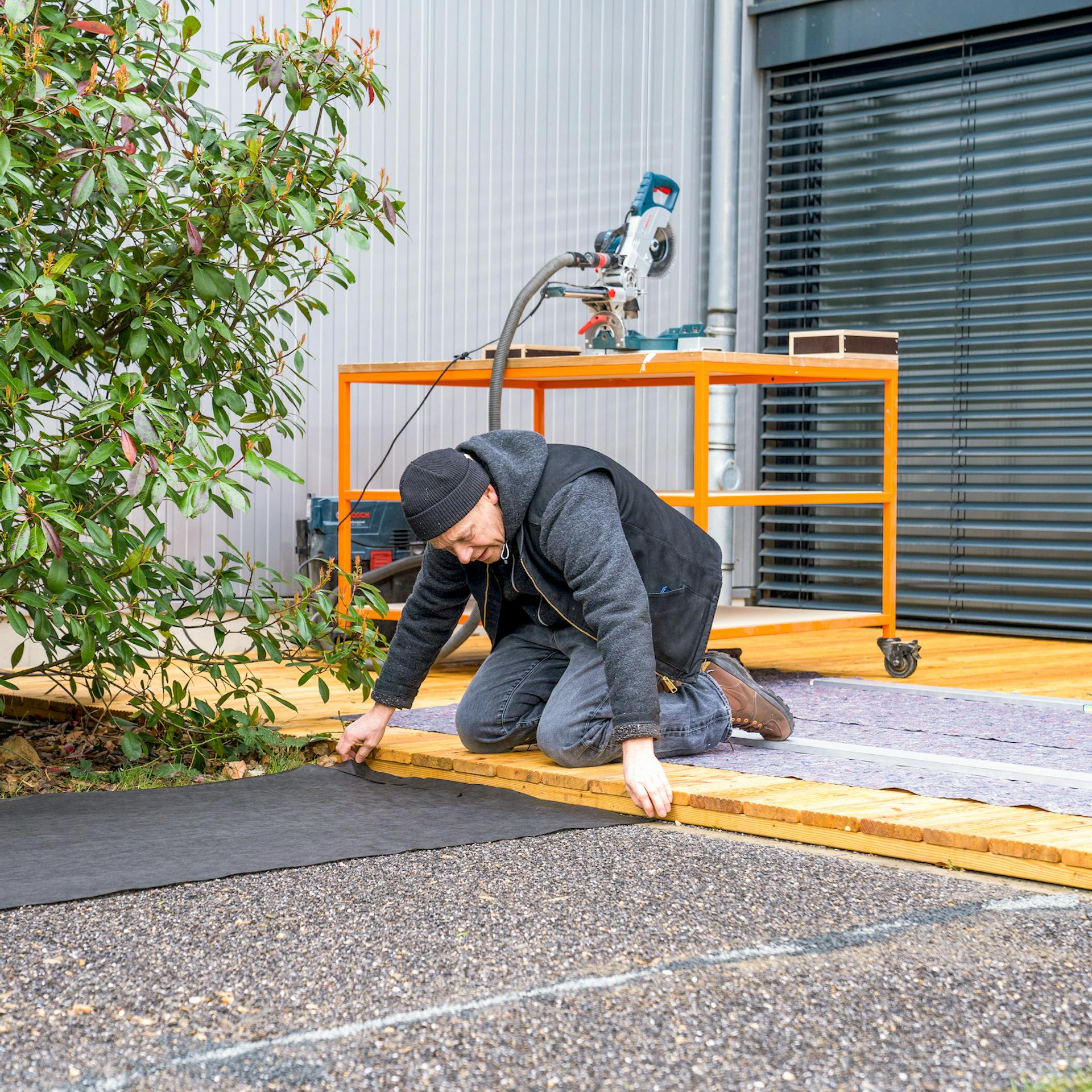 Ein Mann hält ein Unkrautvlies an eine Terrasse.