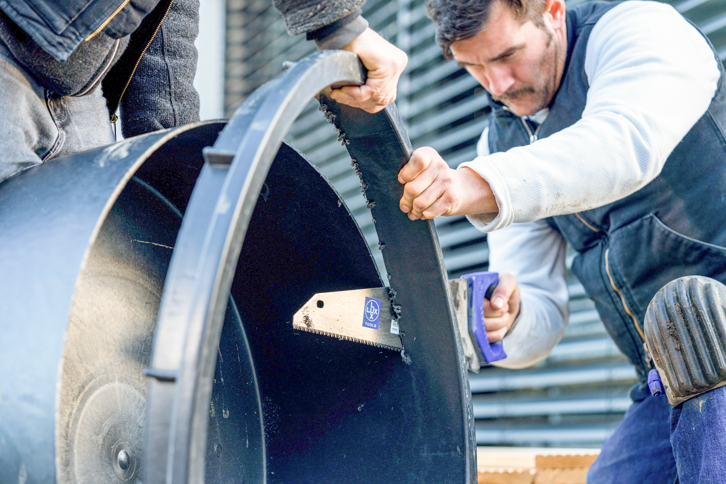 Un uomo sega il bordo di una vasca di plastica.