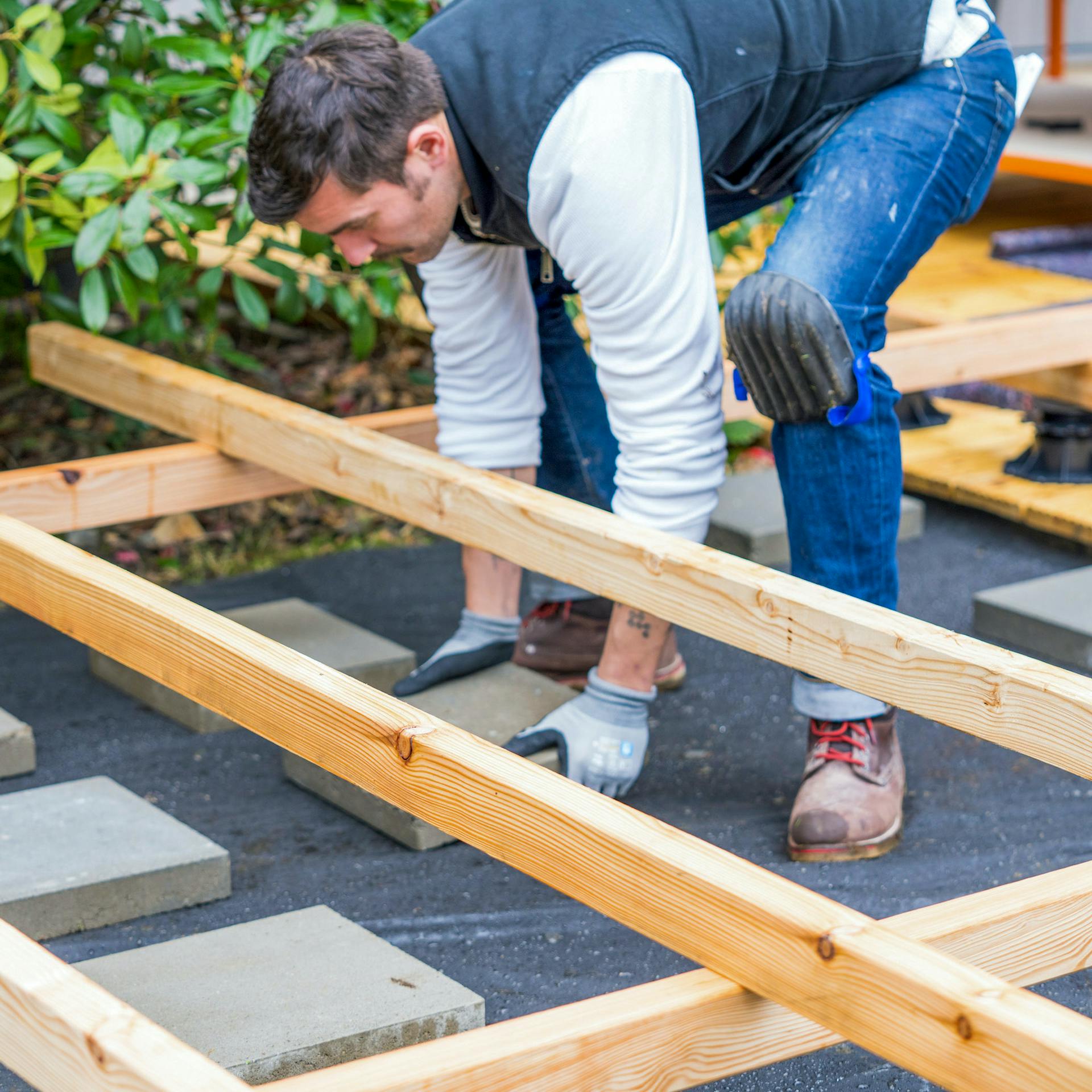 Mann schiebt Betonplatten unter eine Terrassen-Unterkonstruktion.