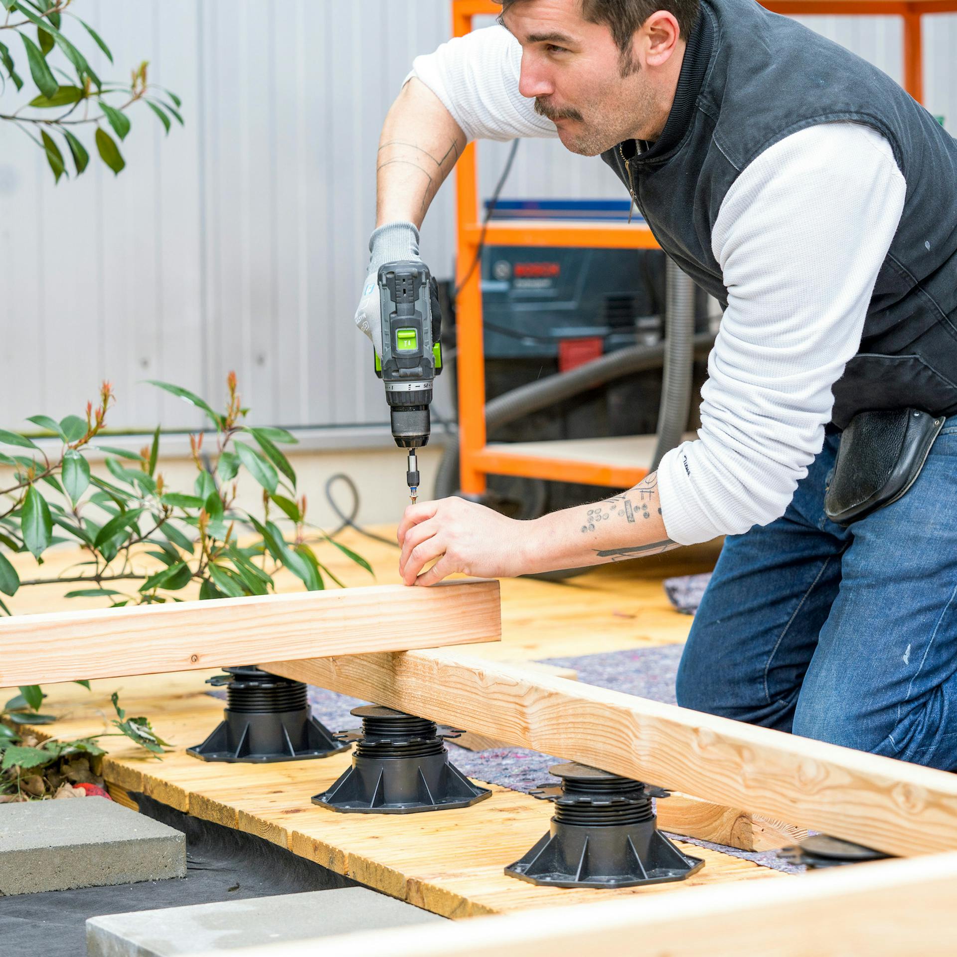 Ein Mann schraubt einen Holzbalken auf eine Terrassen-Unterkonstruktion.