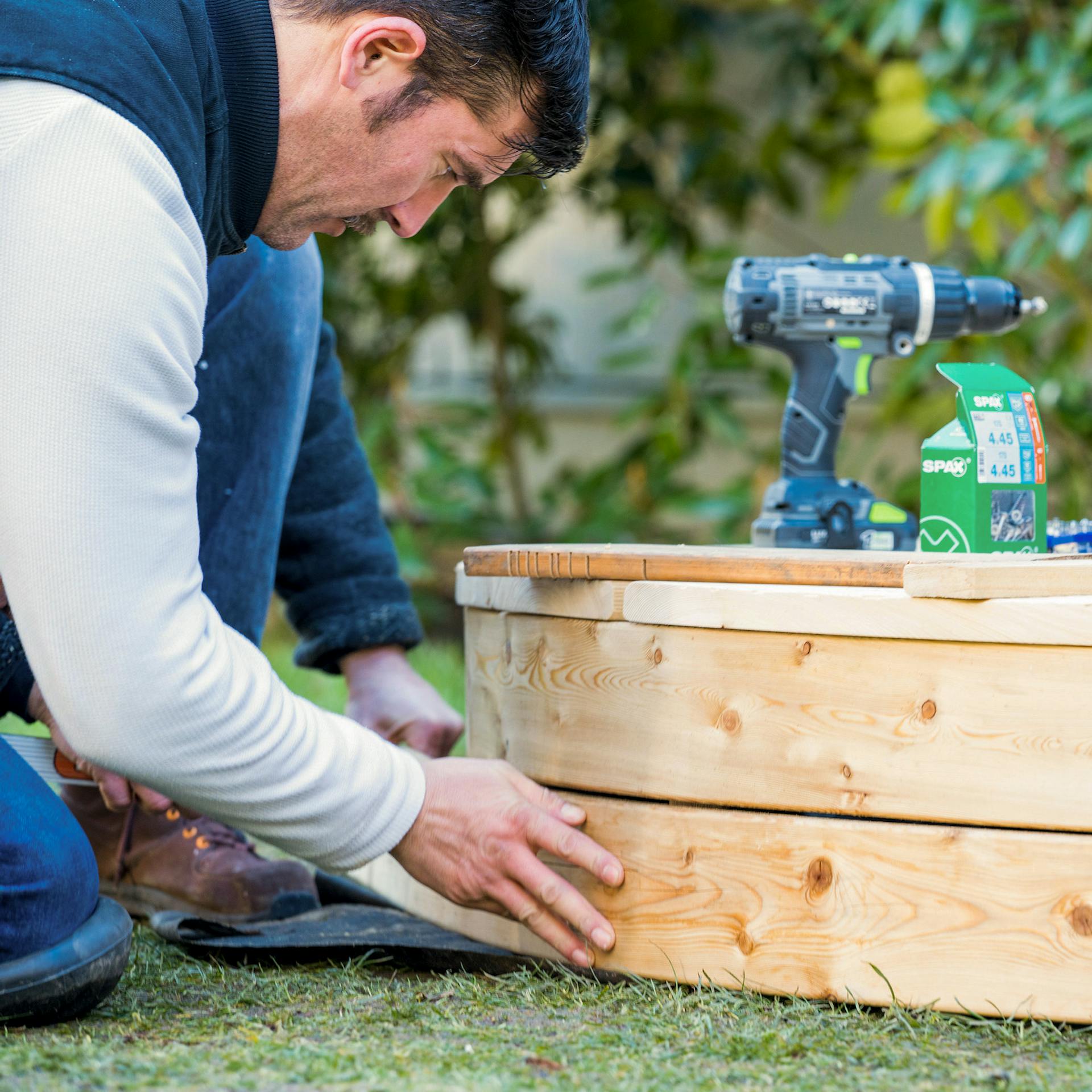 Ein Mann schraubt eine Verblendung an eine Terrasse.