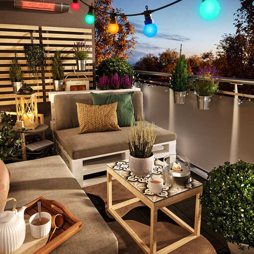 Palettencouch Bankig steht auf einem Balkon der mit Lichterketten geschmückt ist und der eine Sprossenwand besitzt an den Pflanzen aufgehängt sind