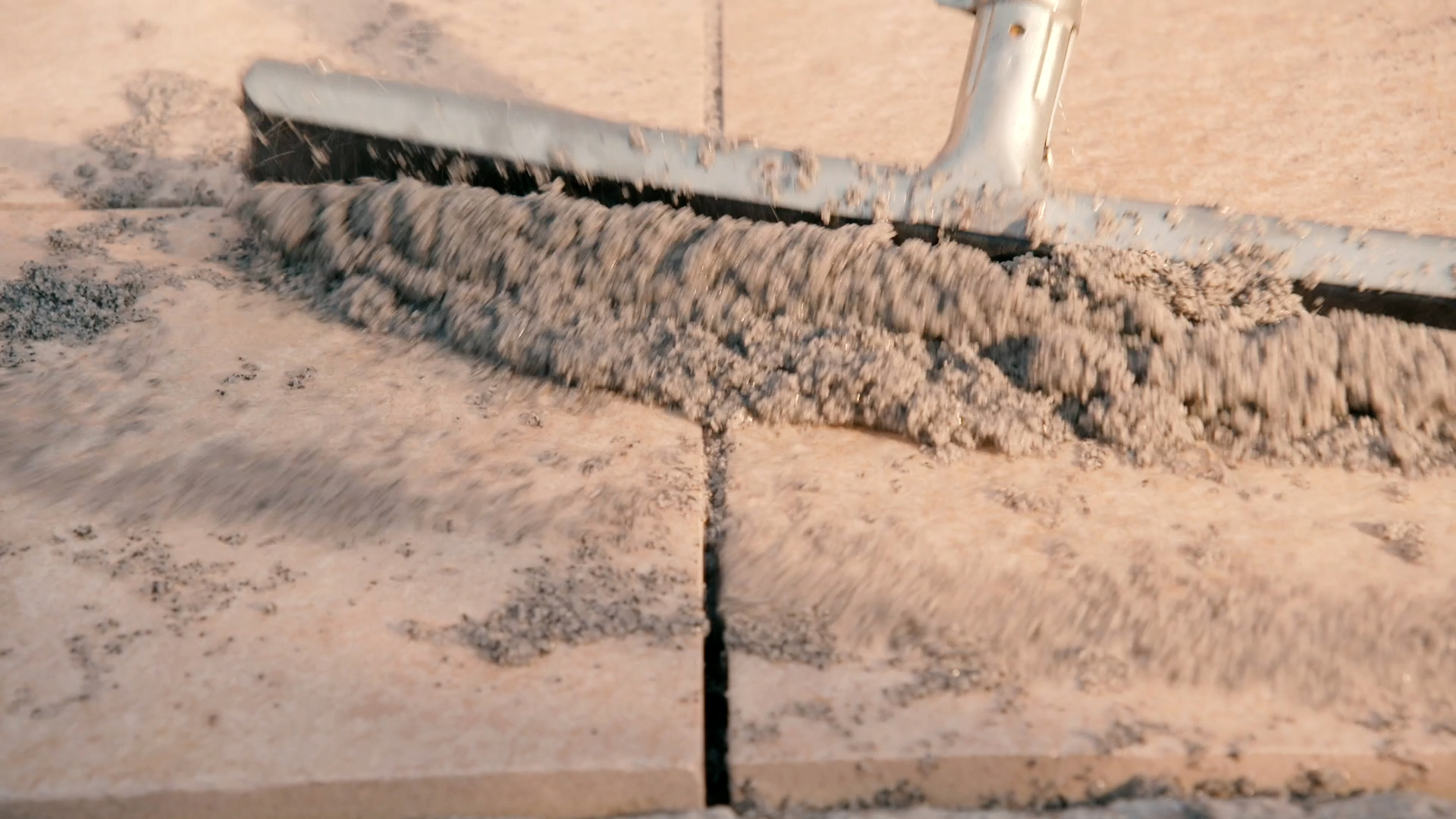 Person verteilt Fugenmasse mithilfe eines Wasserschiebers zwischen Terrassenplatten.