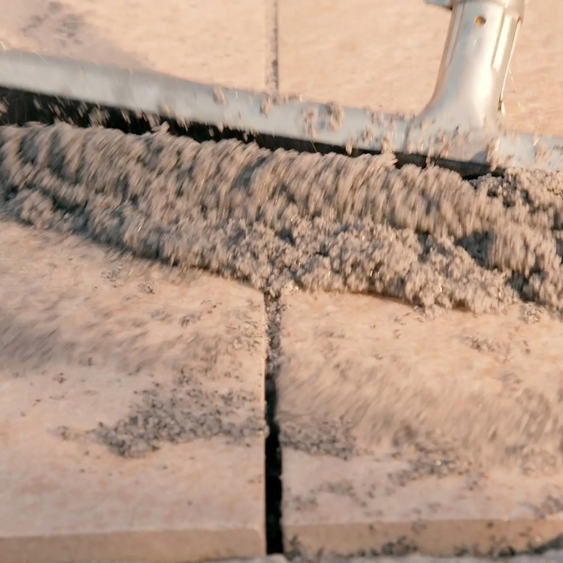 Person verteilt Fugenmasse mithilfe eines Wasserschiebers zwischen Terrassenplatten.