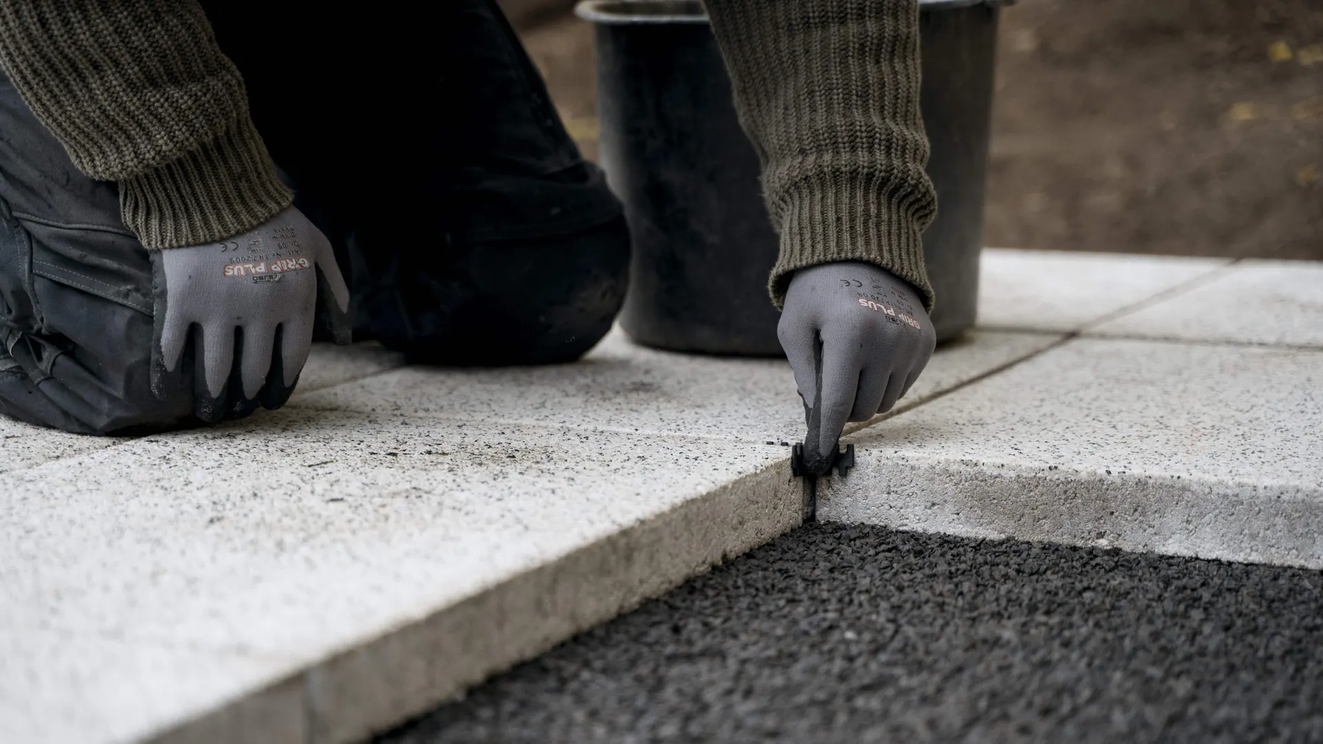 Person setzt Fugenkreuze zwischen Terrassenplatten zum Verfugen.