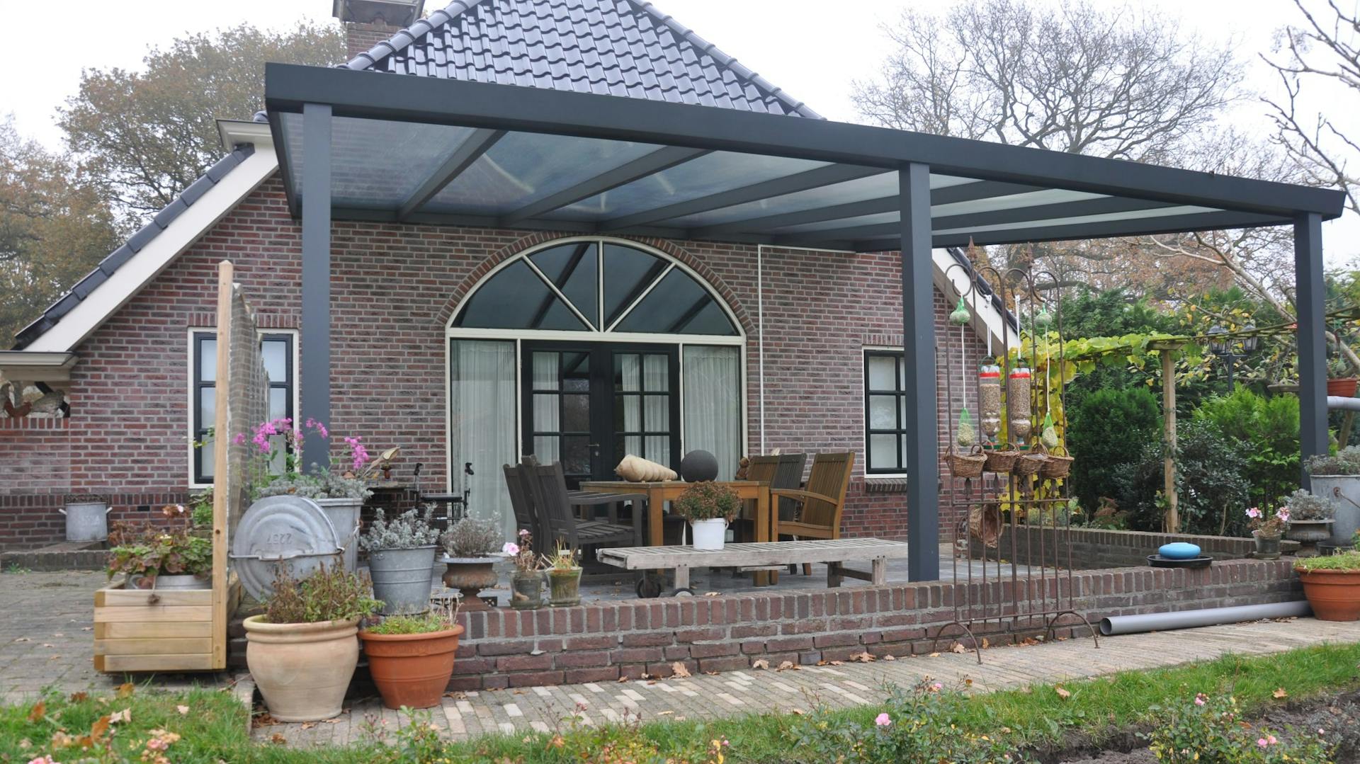 Terrasse im Garten mit einer dunklen Terrassenüberdachung an Hausfassade mit roten Ziegelsteinen