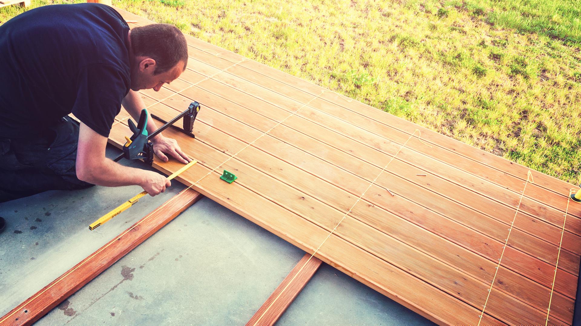 Un uomo misura il listello di legno di una terrazza.