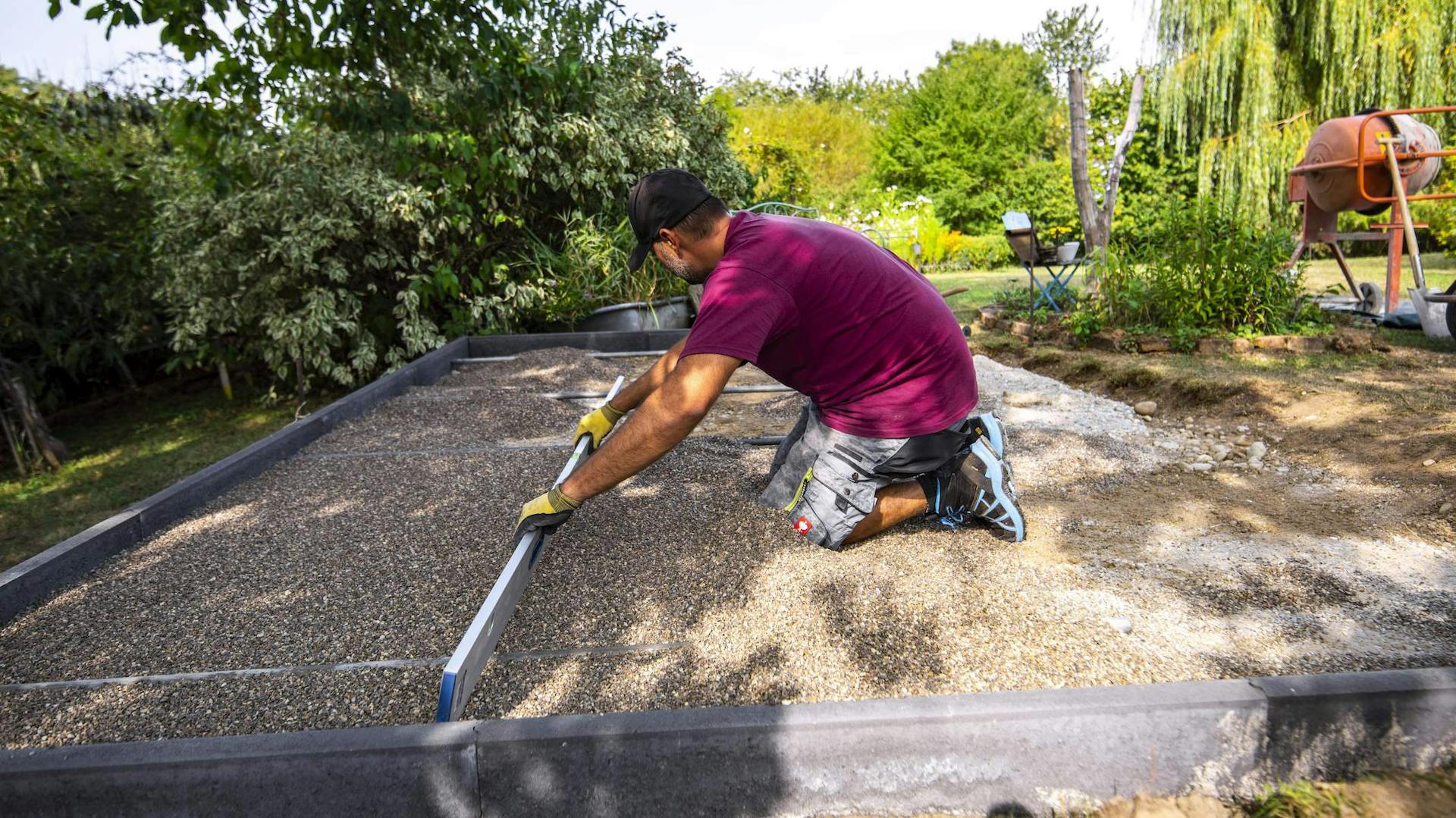 Heimwerker zieht Kiesschicht als Fundament glatt.