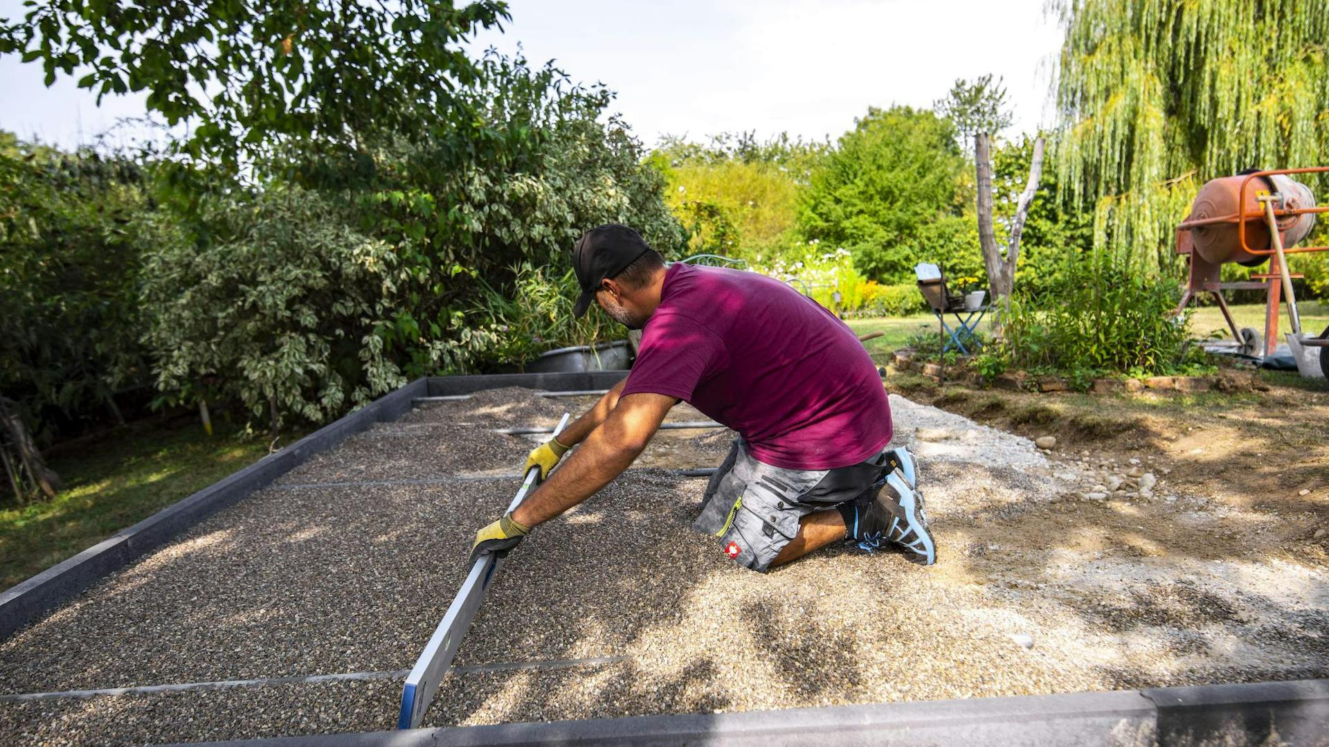 Mann zieht eine Ausgleichsschicht aus Splitt gerade