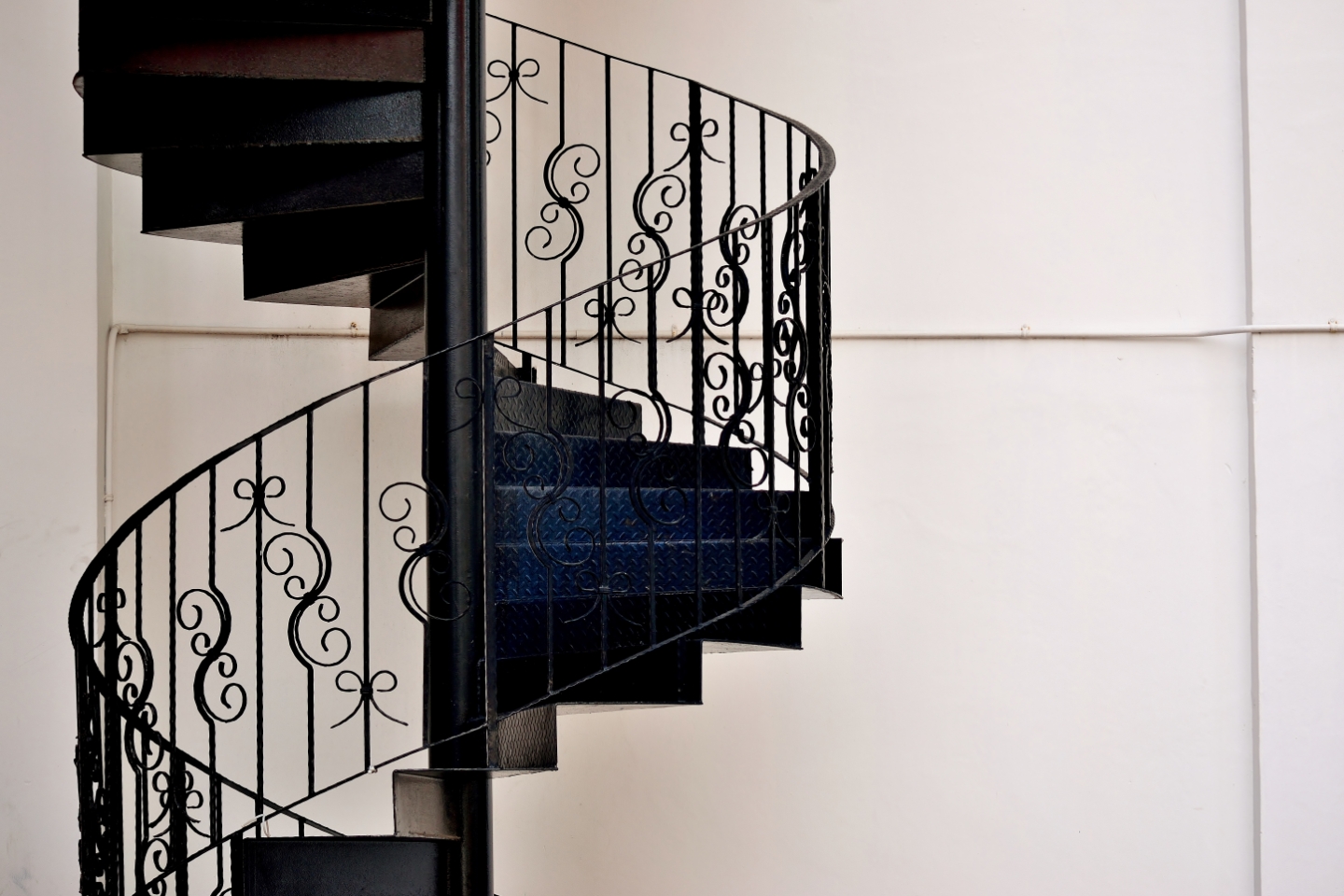 Nahaufnahme einer Wendeltreppe aus schwarzem Metall und verspieltem Geländer vor einem weißen Hintergrund.