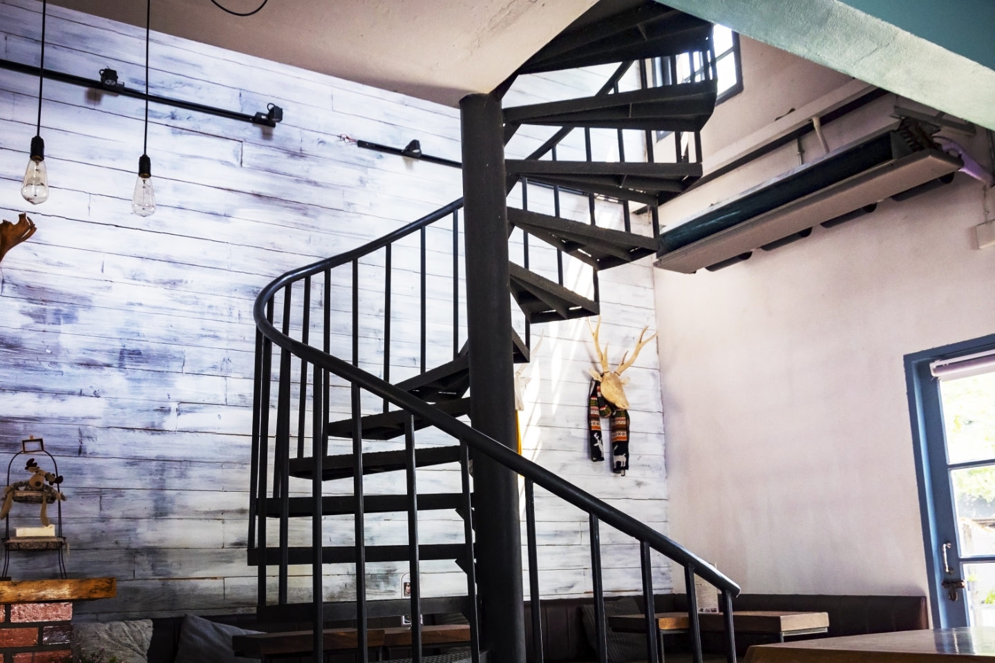 Es ist ein moderner Raum zu sehen. In der Mitte des Raumes steht eine gewendelte Treppe aus schwarzem Metall mit Geländer.