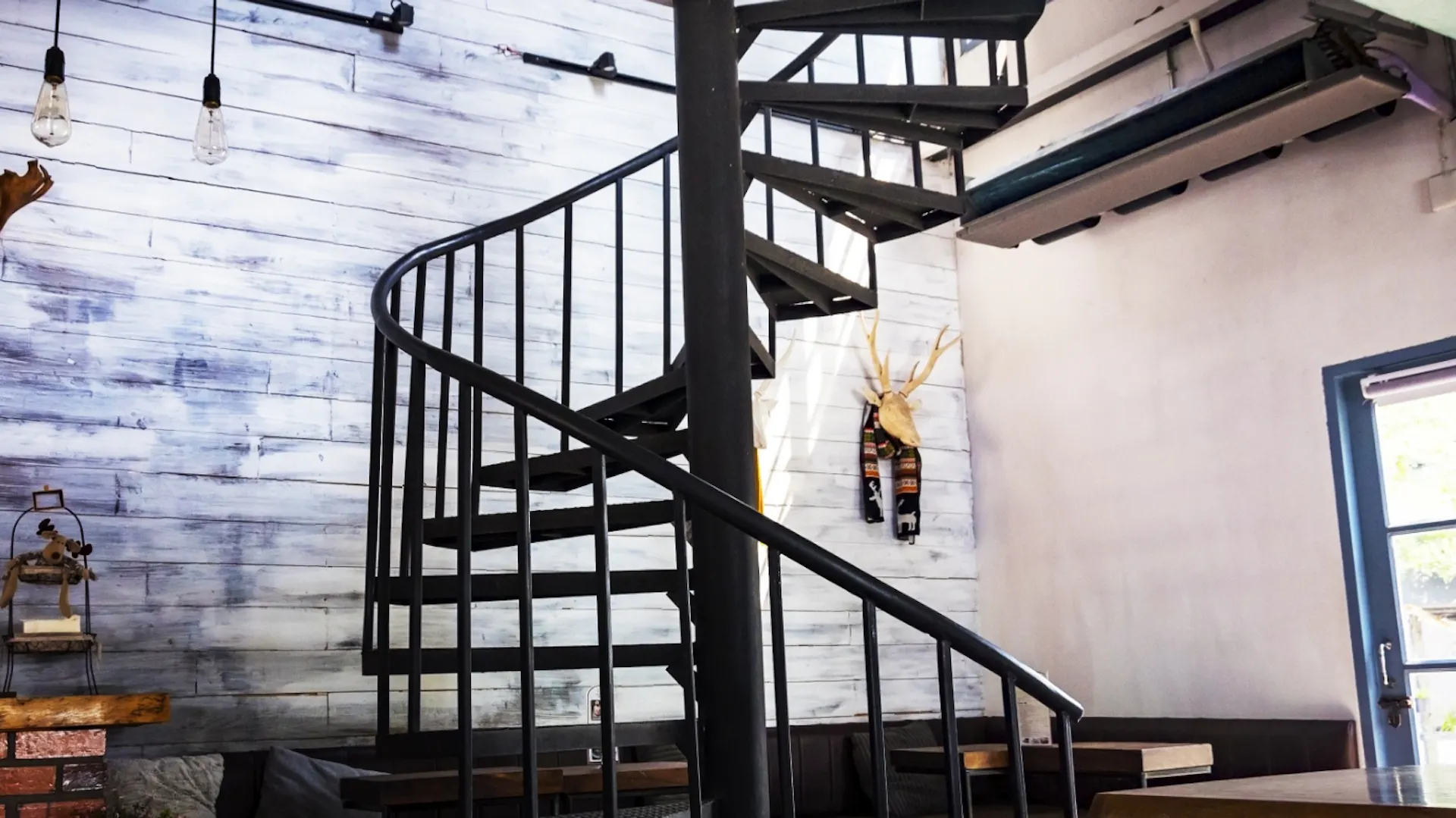 Es ist ein moderner Raum zu sehen. In der Mitte des Raumes steht eine gewendelte Treppe aus schwarzem Metall mit Geländer.