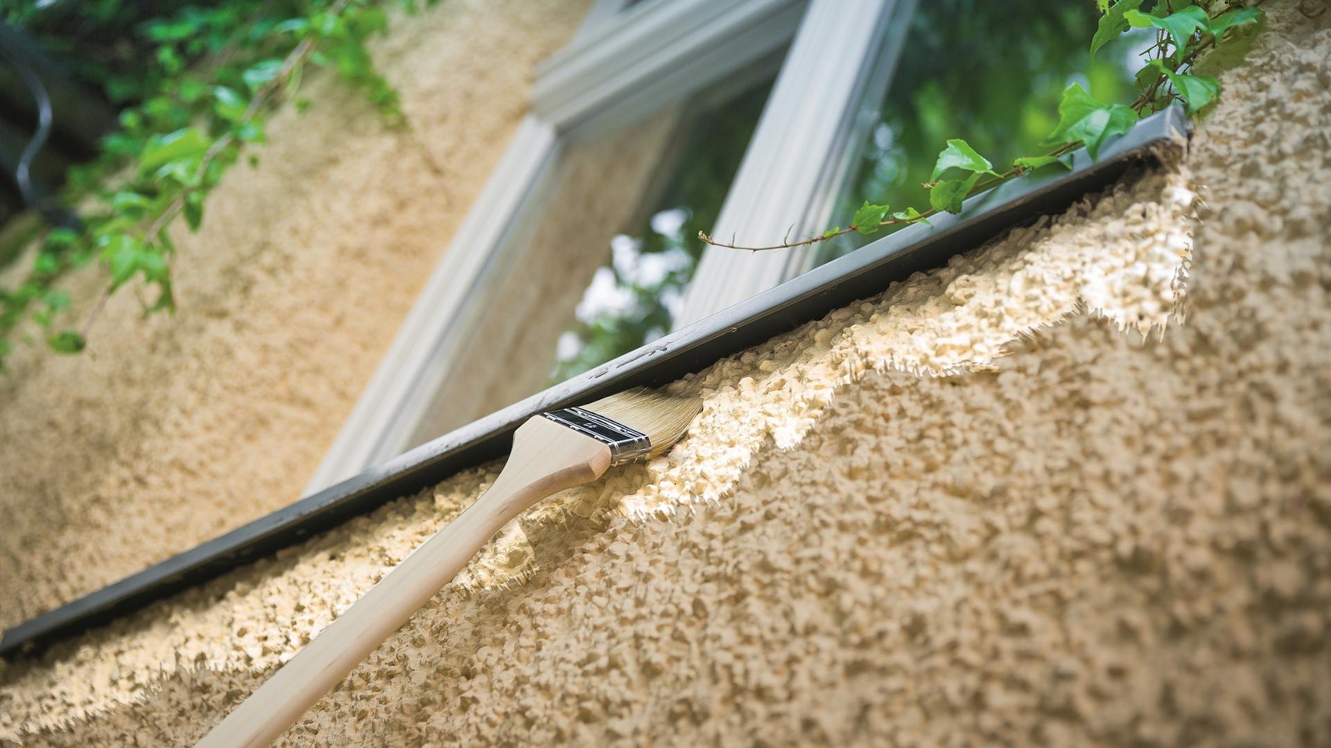 Fassade wird mit einem Pinsel unter einem Fenster gestrichen.