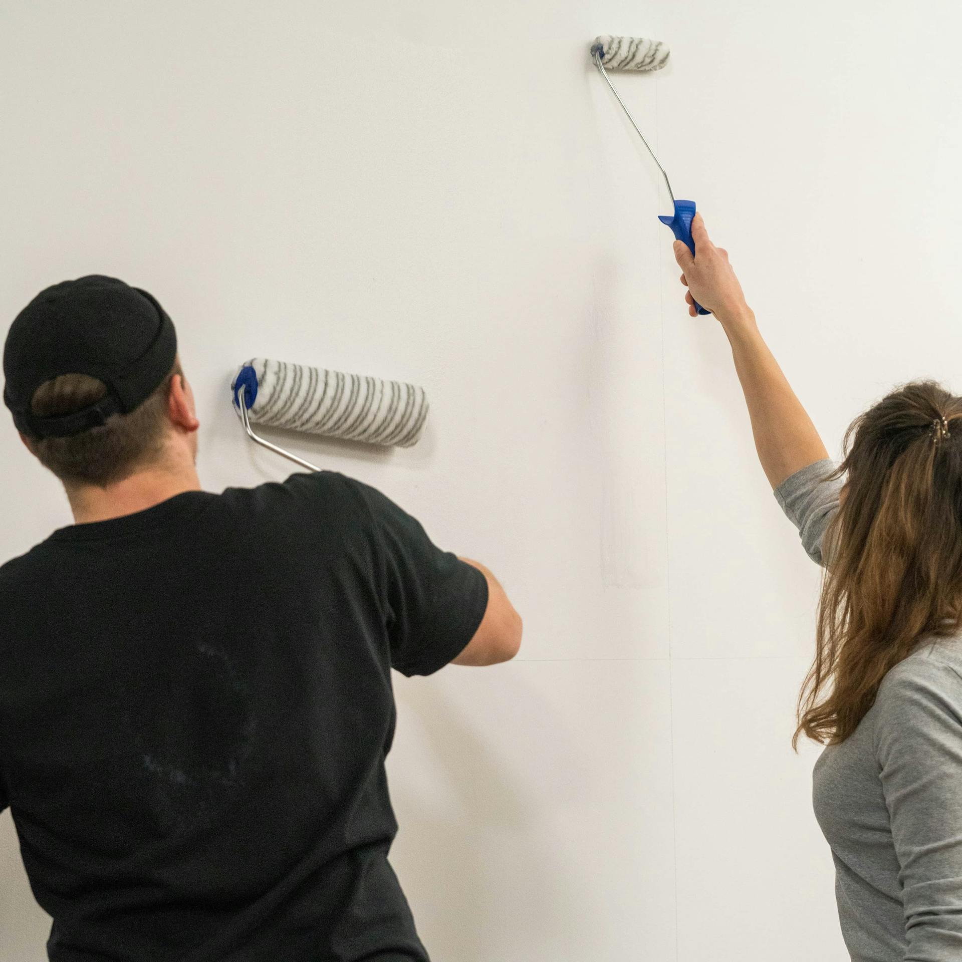 Zwei Personen tragen Tapetenkleister auf gereinigte Wand auf.
