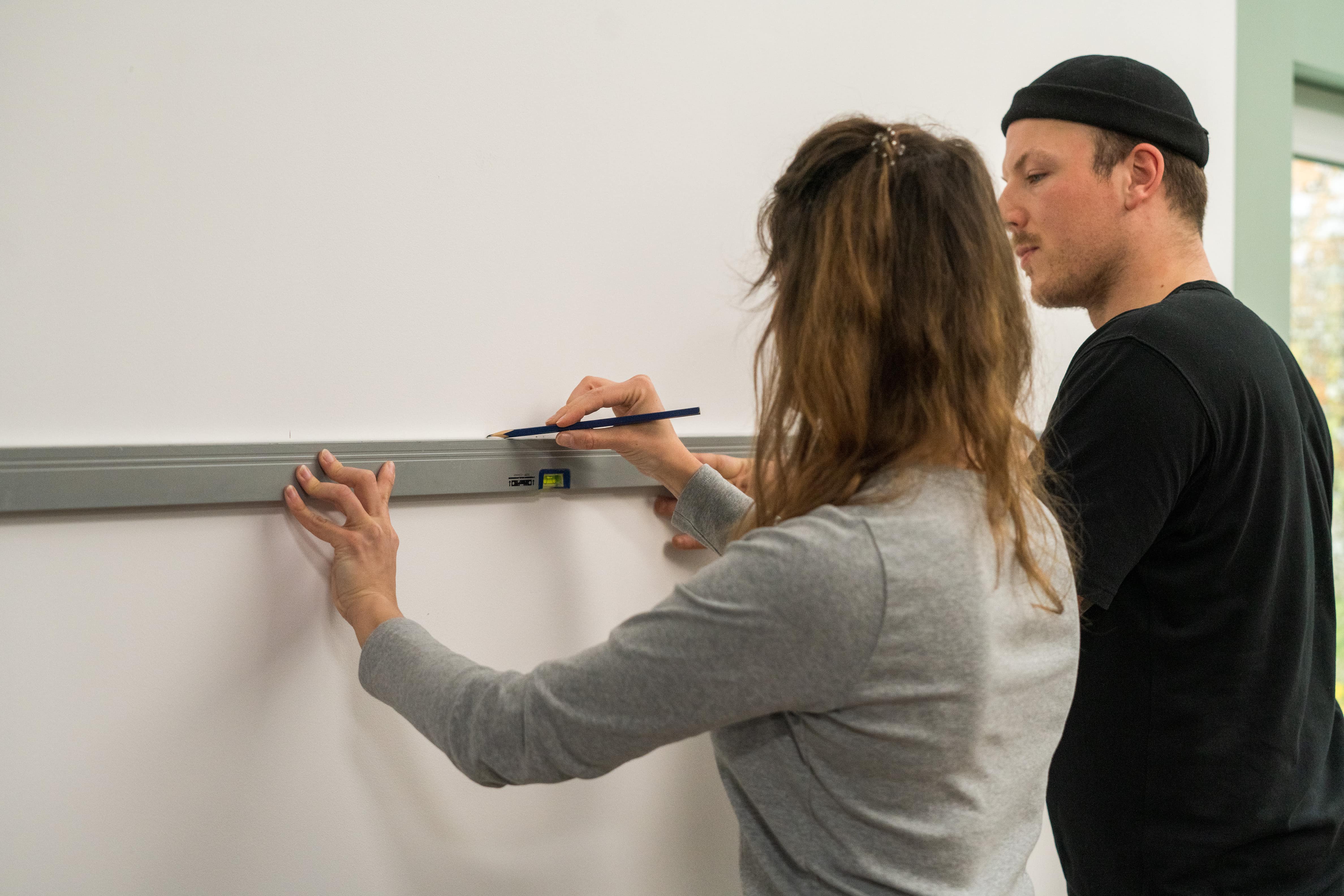 Zwei Personen zeichnen mithilfe einer Wasserwaage eine Hilfslinie an eine Wand.