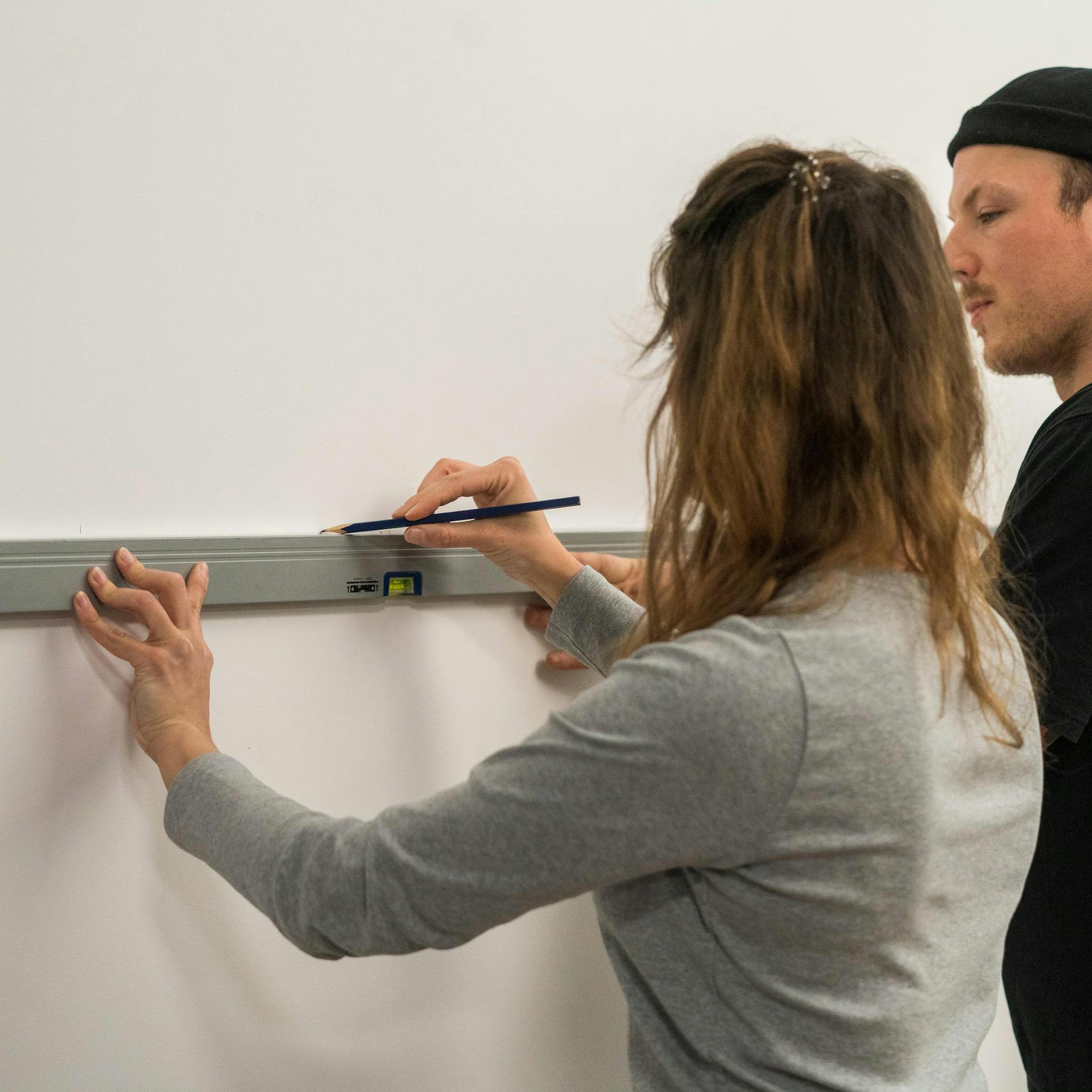 Zwei Personen zeichnen mithilfe einer Wasserwaage eine Hilfslinie an eine Wand.
