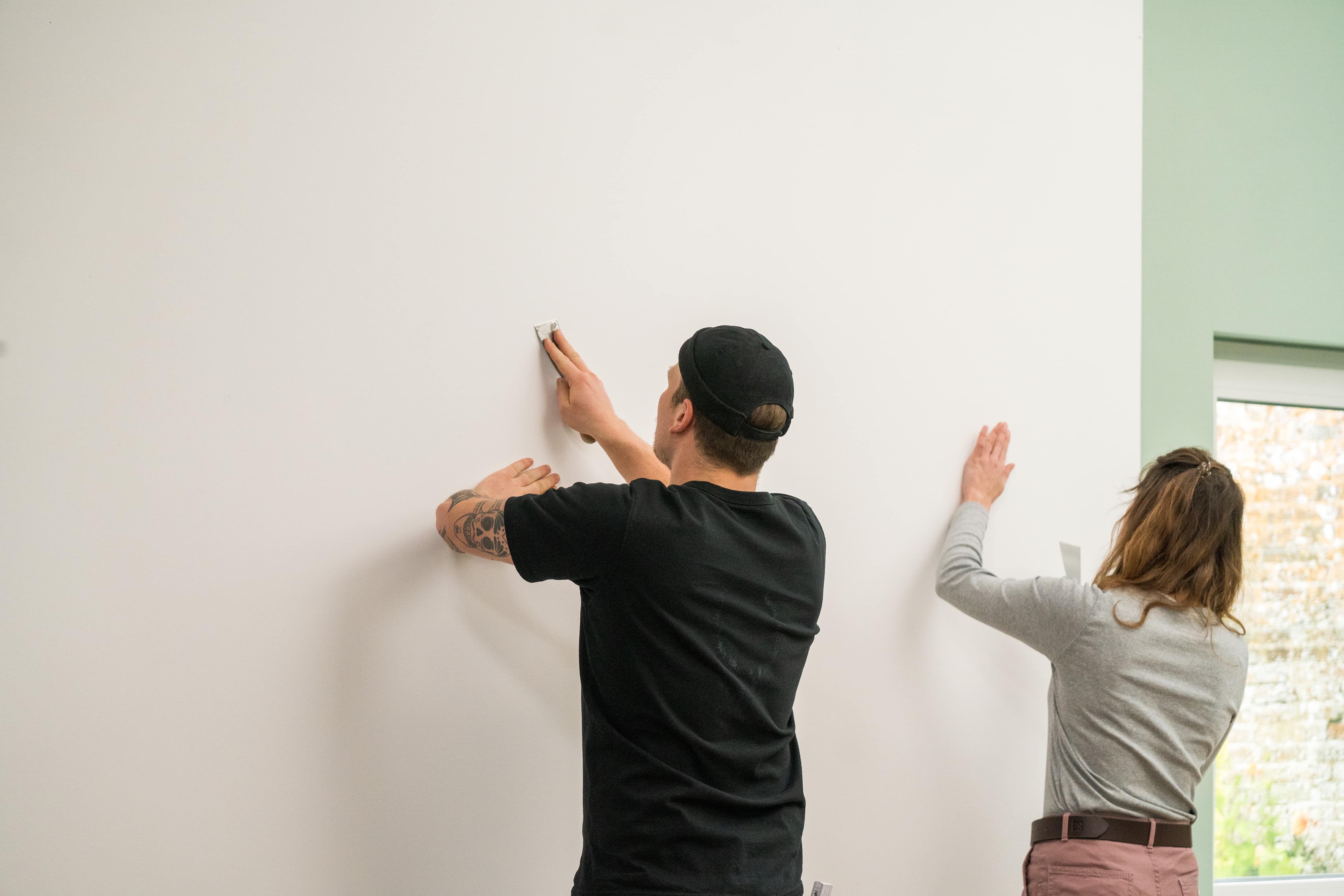 Zwei Personen reinigen eine Wand vor dem Tapezieren
