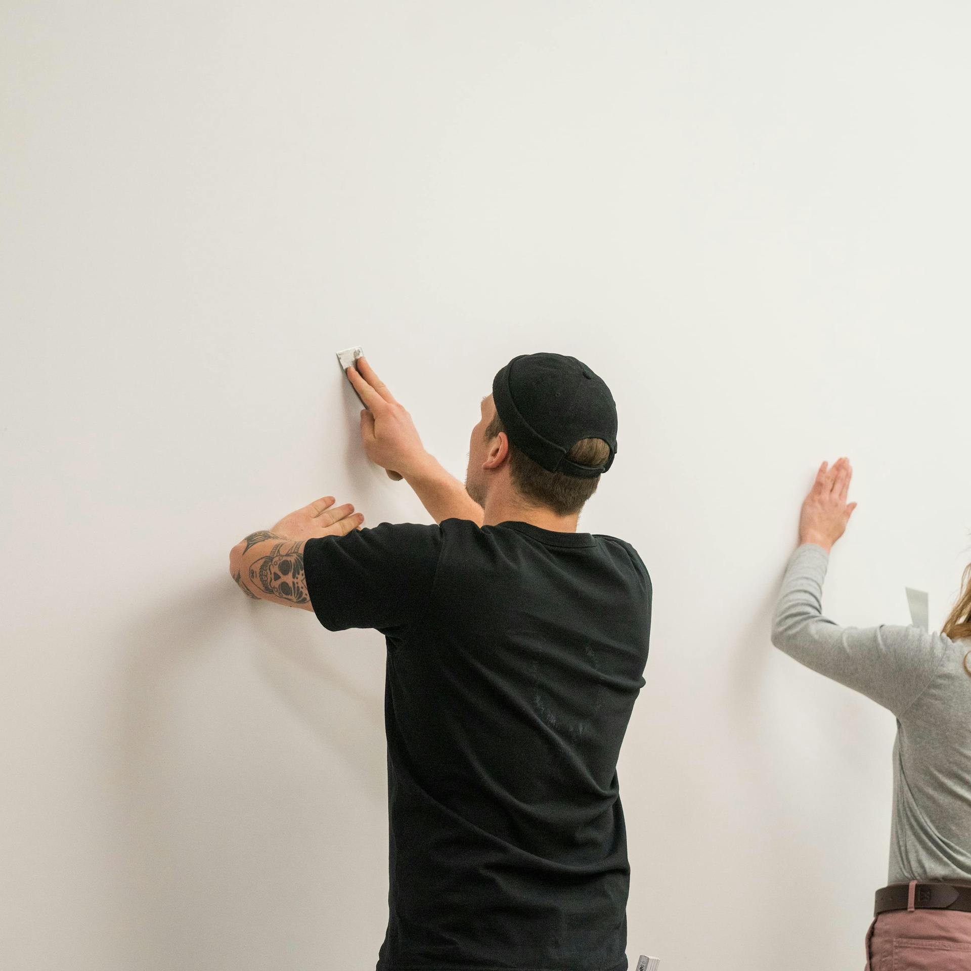 Zwei Personen reinigen eine Wand vor dem Tapezieren