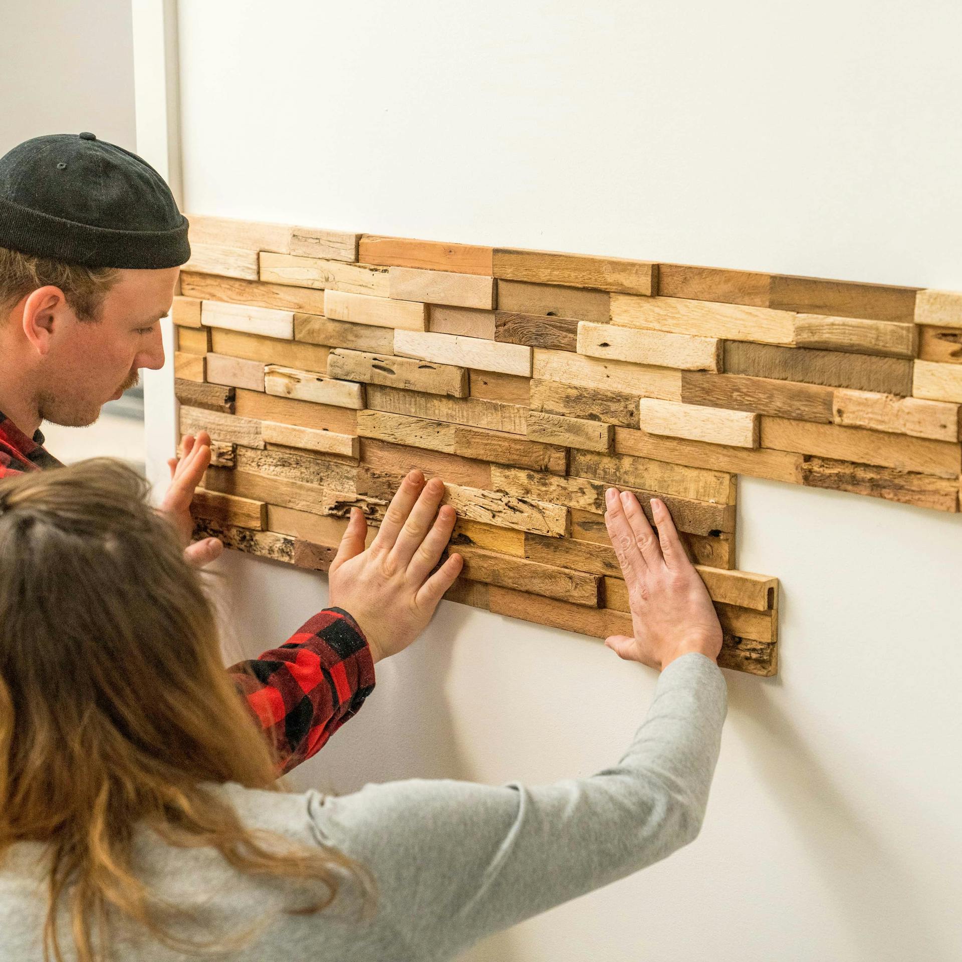 Zwei Personen bringen weitere Holzverblender an Wand an.