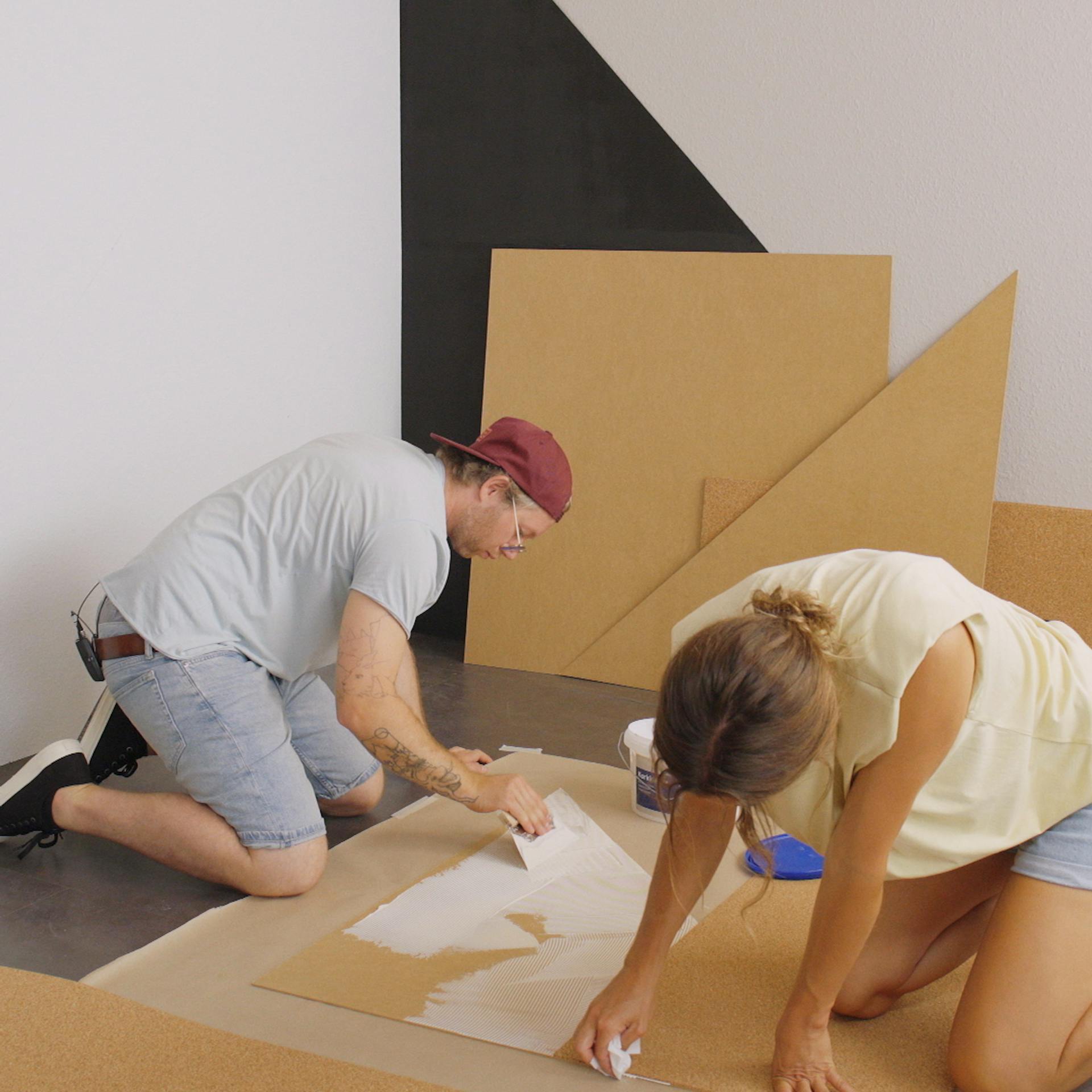 Zwei Heimwerker verkleben Kork mit Trägerplatte für Korkwand