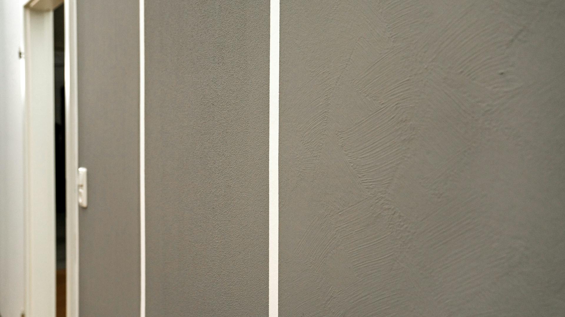 Das Bild zeigt eine Wand, auf die Rollputz aufgetragen und in breiten Streifen dunkelgrau gestrichen wurde.