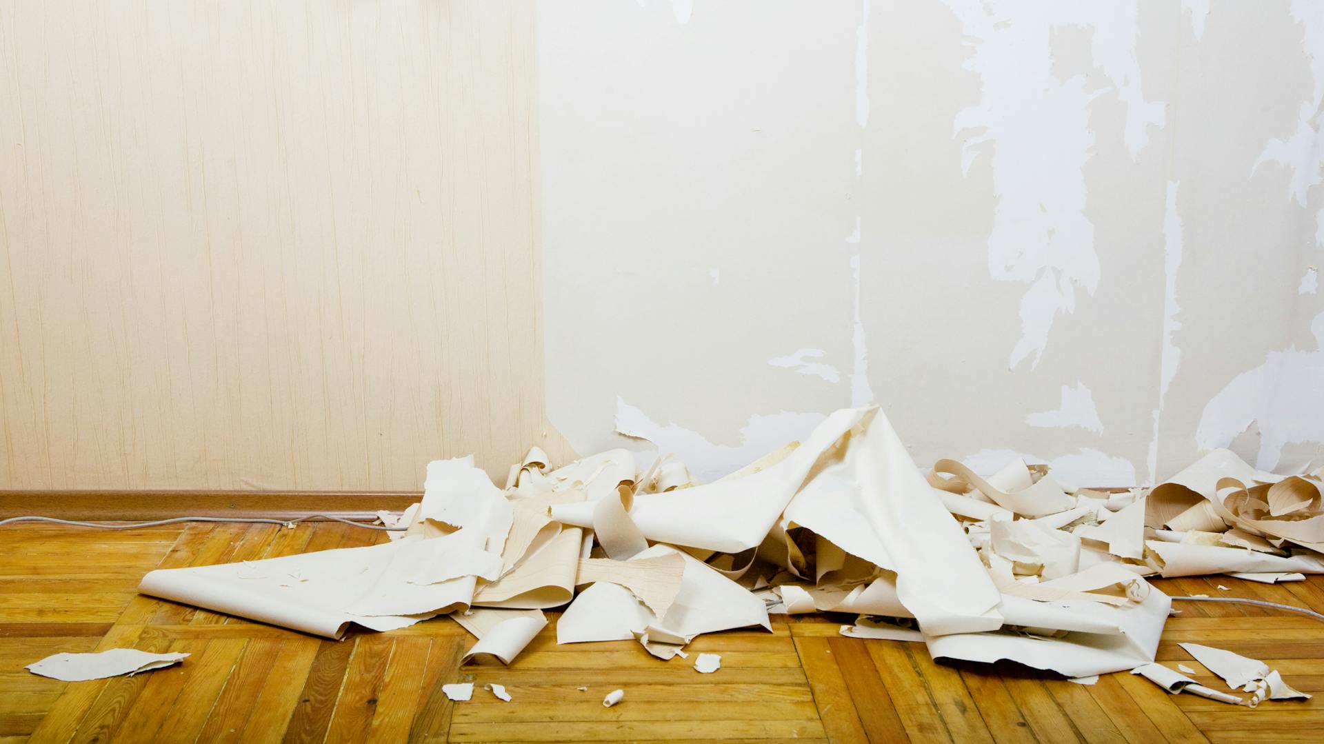 Tapetenreste liegen auf Boden neben Wand.