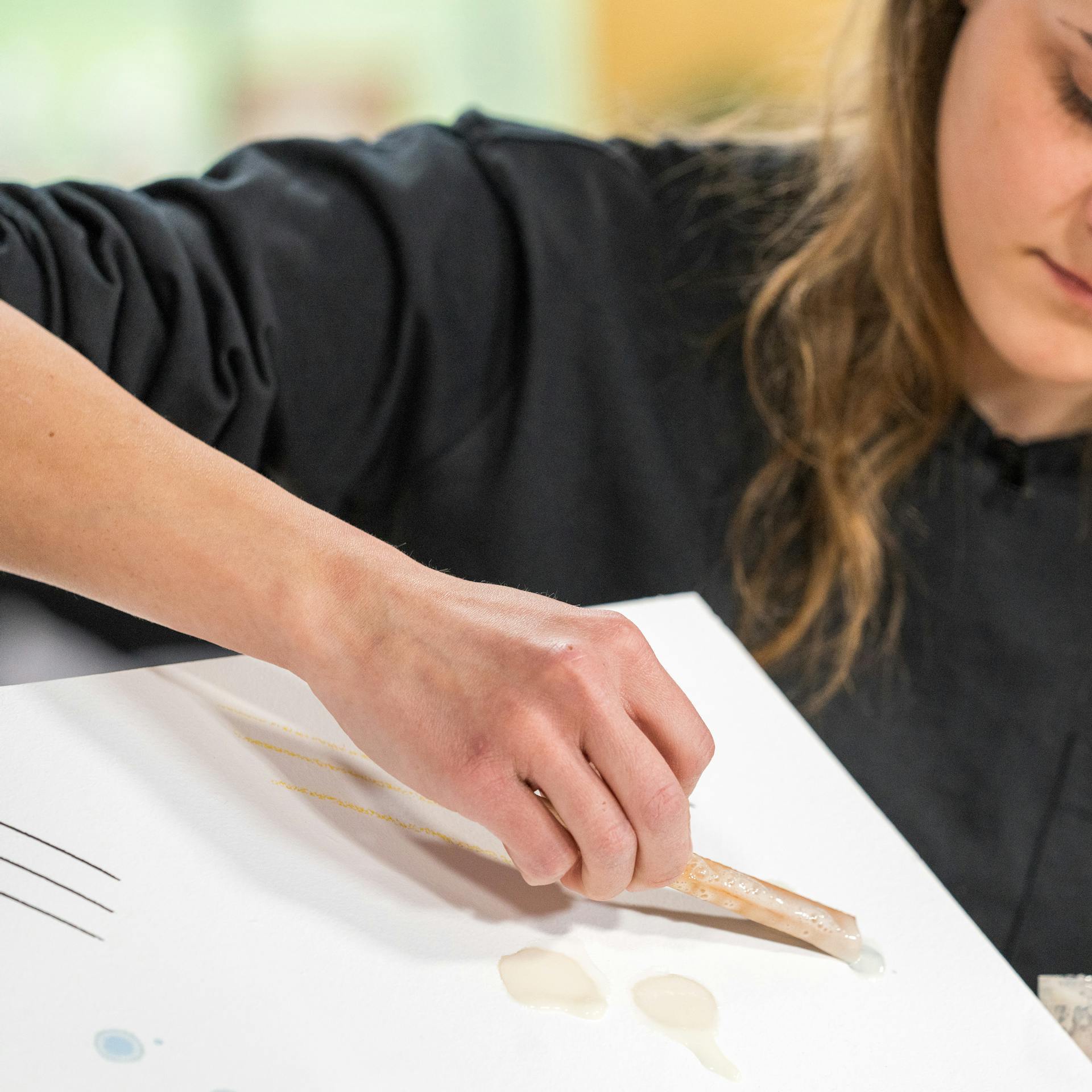 Pracovníčka ukazuje ako vyčistiť tapetu pomocou drevenej špachtle a zmesy kypriaceho prášku a vody.