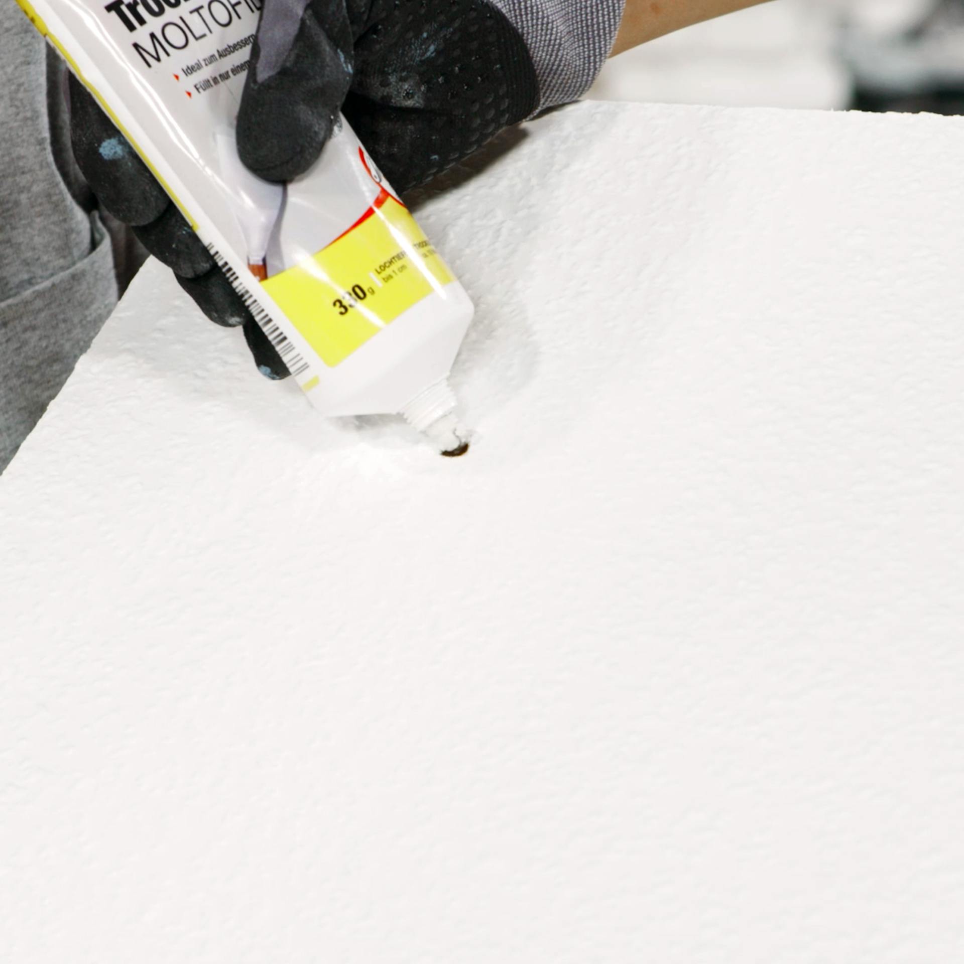 Pracovníčka vypĺňa dieru v tapete hotovou stierkou z tuby.