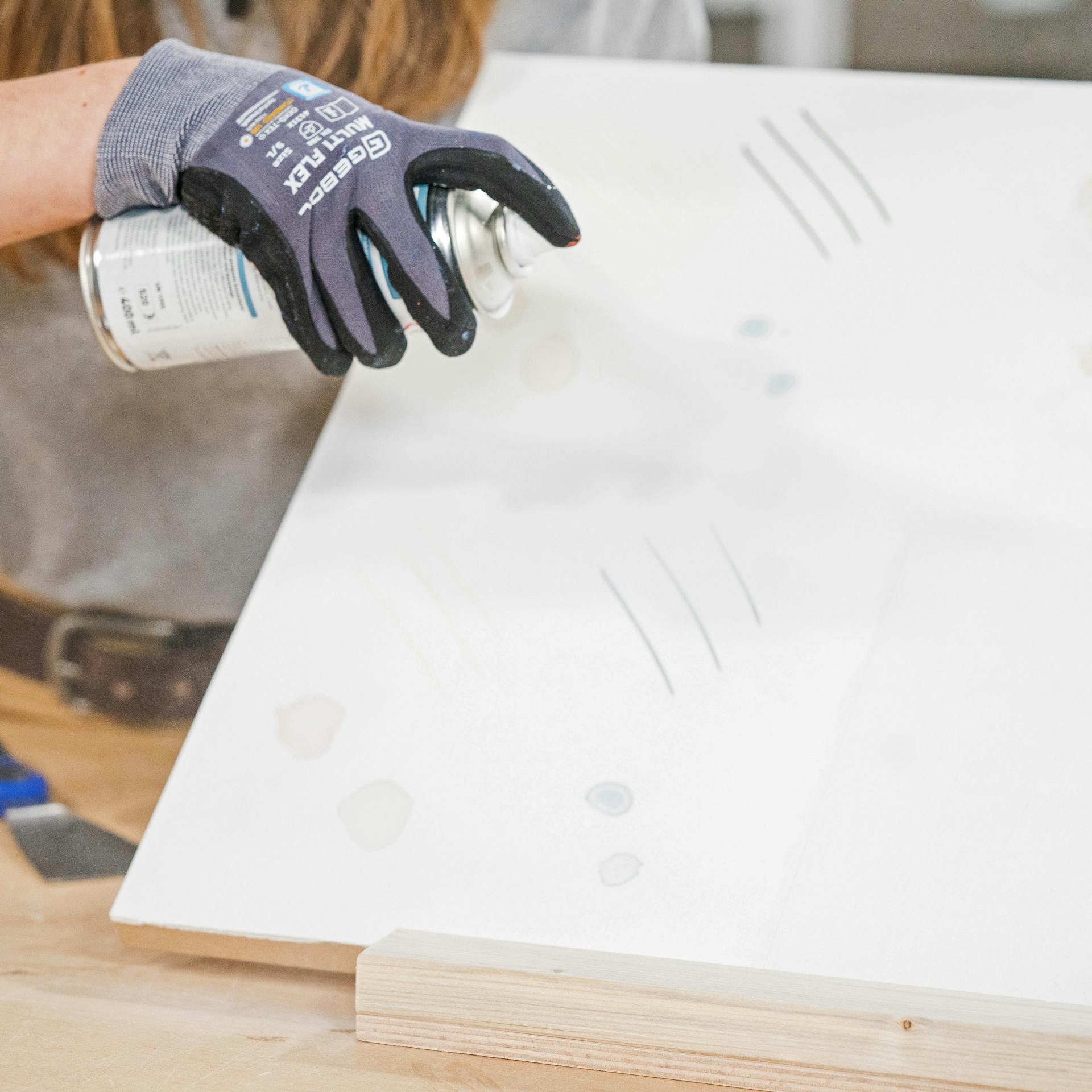 Pracovníčka v rukaviciach aplikuje na vzorovanú tapetu izolačný sprej.