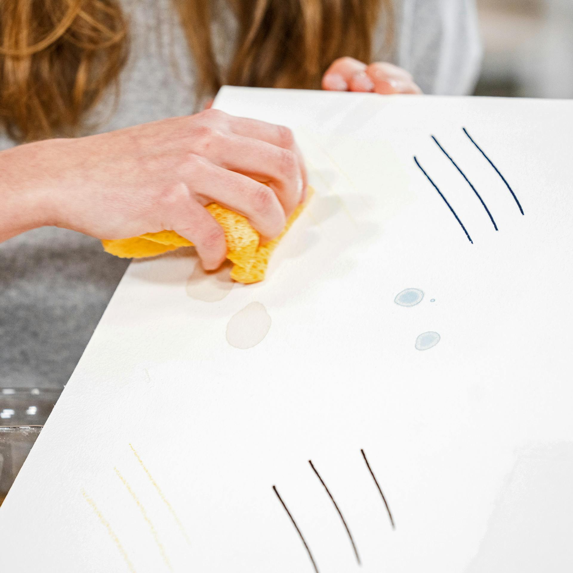 Pracovníčka na testovacej tapete ukazuje, ako odstrániť škvrny z tapety žltou handričkou.