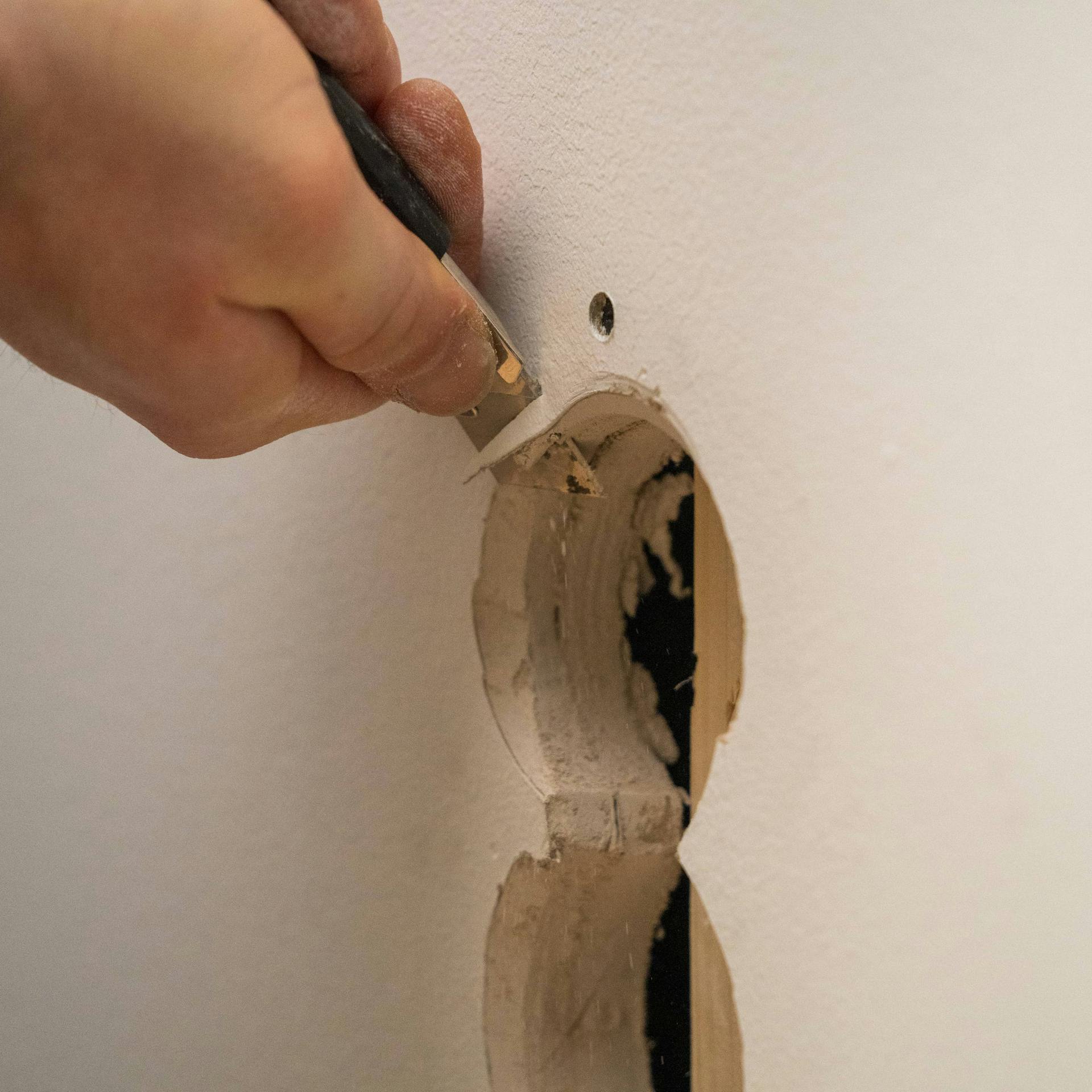 Jemand entgratet ein Loch in einer Trockenbauwand.