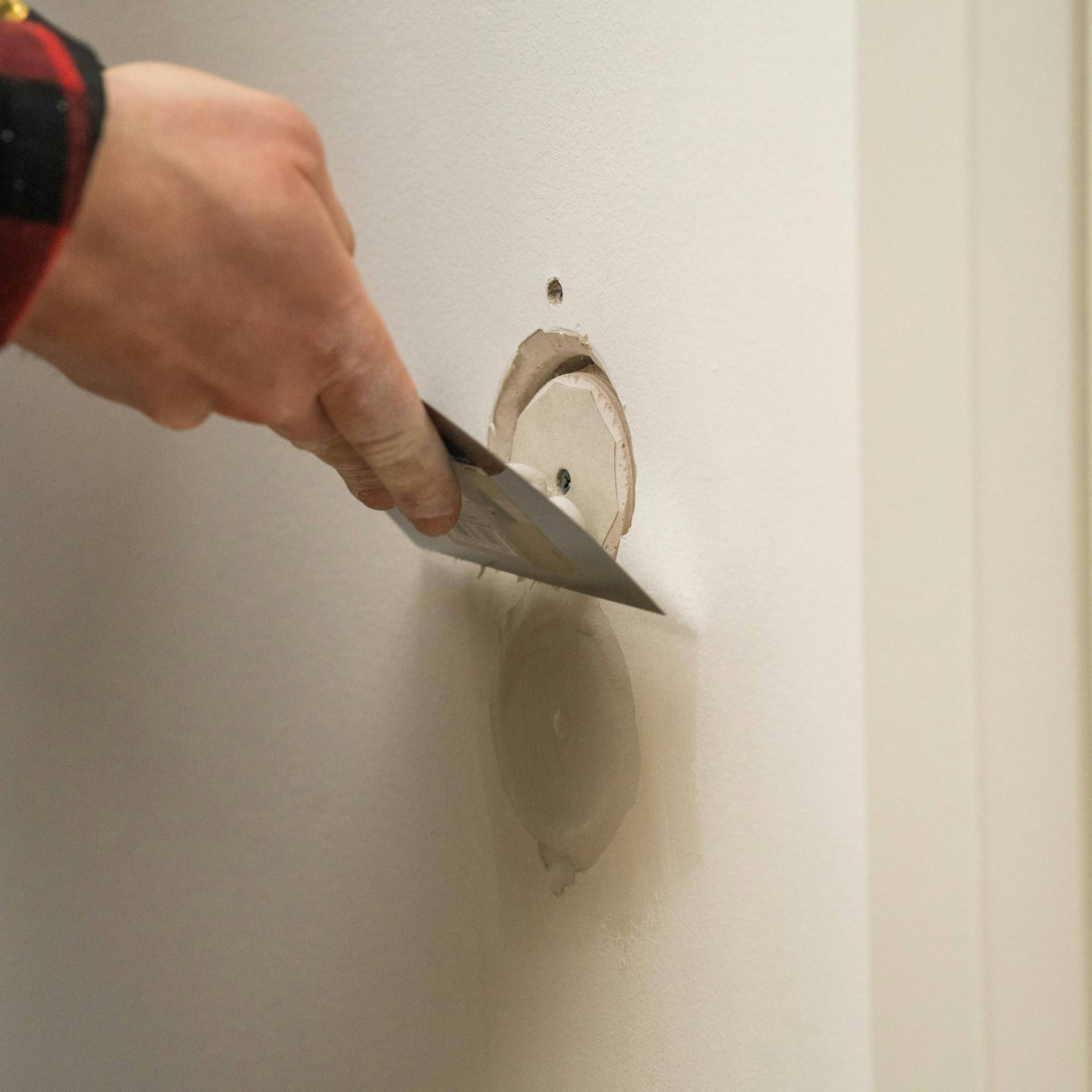 Jemand füllt Löcher in einer Trockenbauwand mit Spachtelmasse.